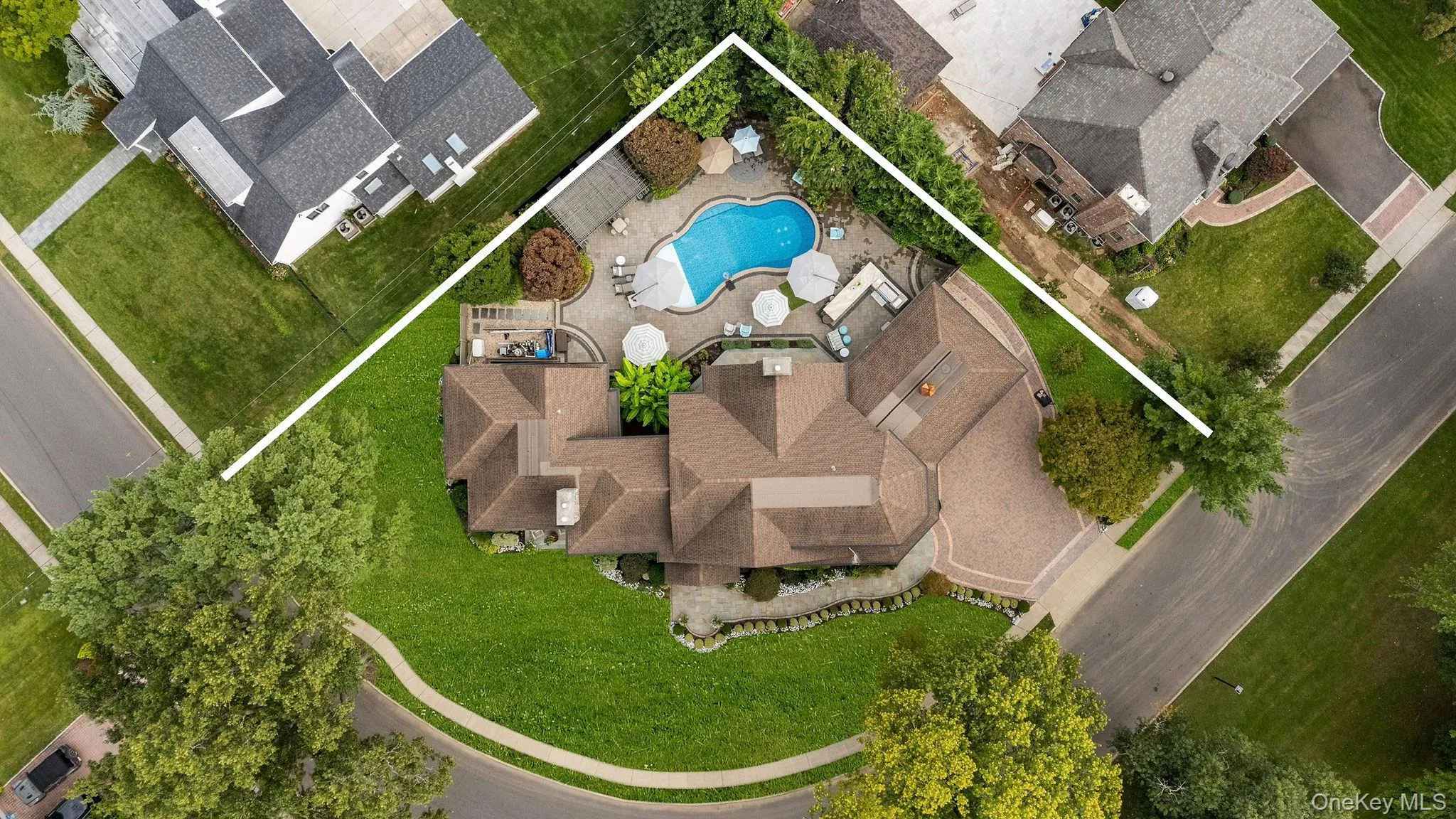 Aerial view featuring a paved driveway, multi-gabled roofline, expansive backyard, in-ground pool, and stone-paver patio Aerial view featuring a paved driveway, multi-gabled roofline, expansive backyard, in-ground pool, and stone-paver patio