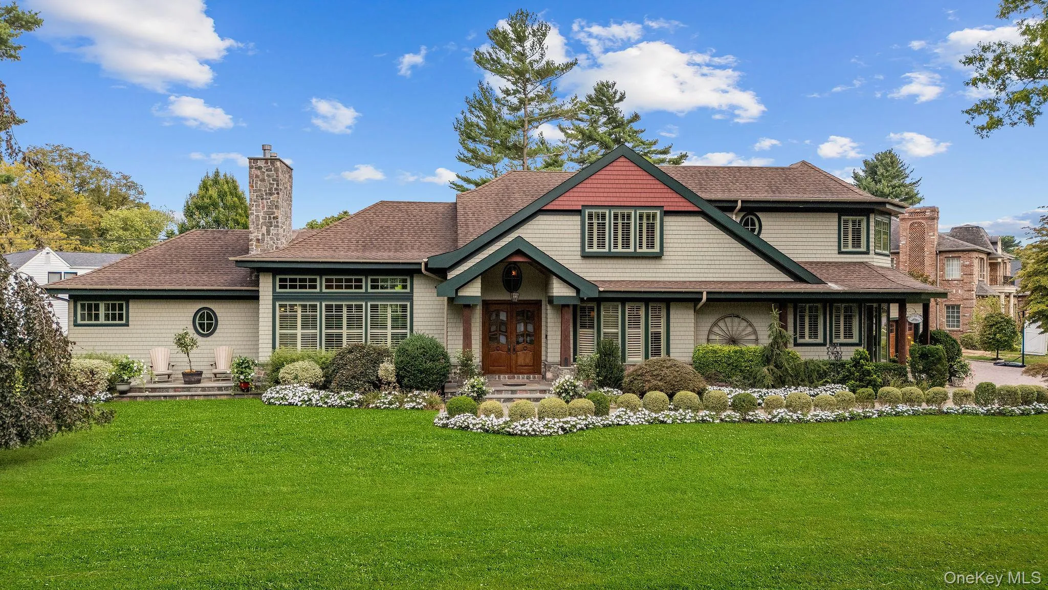 Multi-gabled exterior featuring light-toned shingle siding, contrasting dark window trim, dual stone chimneys, and a covered entryway with double wood-framed doors Multi-gabled exterior featuring light-toned shingle siding, contrasting dark window trim, dual stone chimneys, and a covered entryway with double wood-framed doors