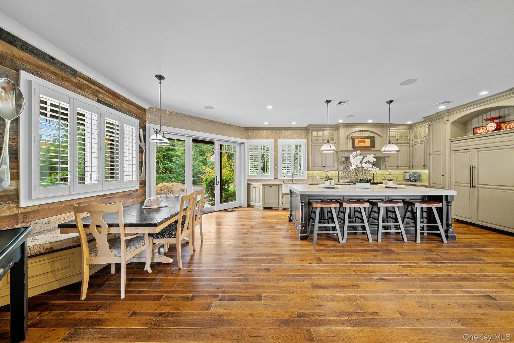 Kitchen featuring a large center island, wood-finish flooring, custom cabinetry, built-in panel-ready refrigerator, and reclaimed wood accent wall Kitchen featuring a large center island, wood-finish flooring, custom cabinetry, built-in panel-ready refrigerator, and reclaimed wood accent wall