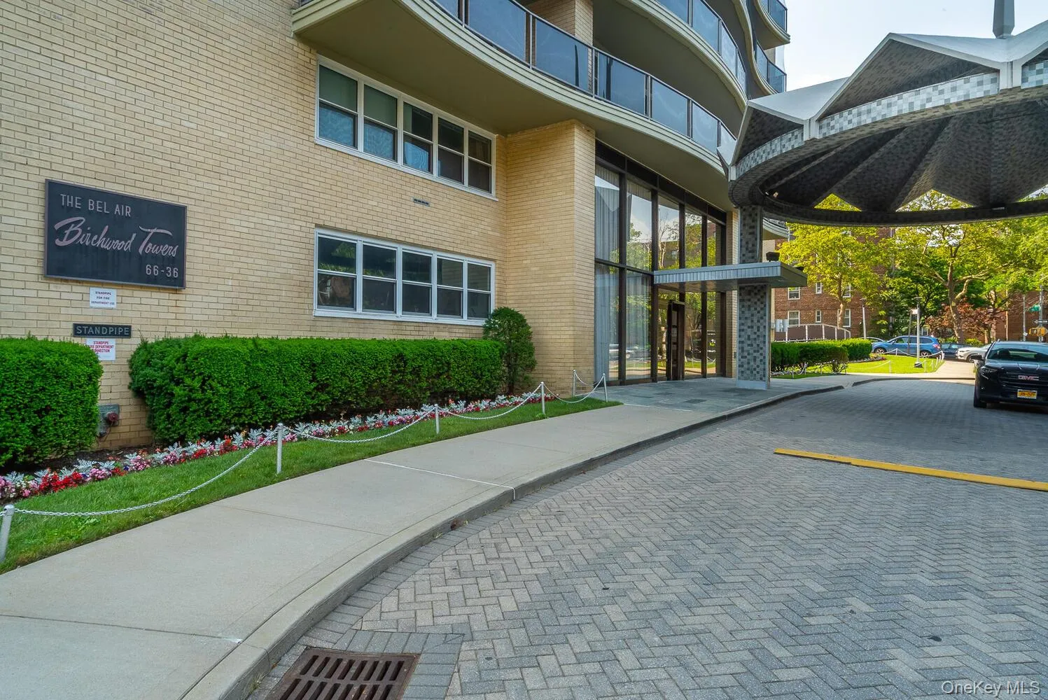 Brick exterior facade featuring a covered porte-cochère, multi-level balconies with glass railings, and a herringbone-patterned paved driveway Brick exterior facade featuring a covered porte-cochère, multi-level balconies with glass railings, and a herringbone-patterned paved driveway