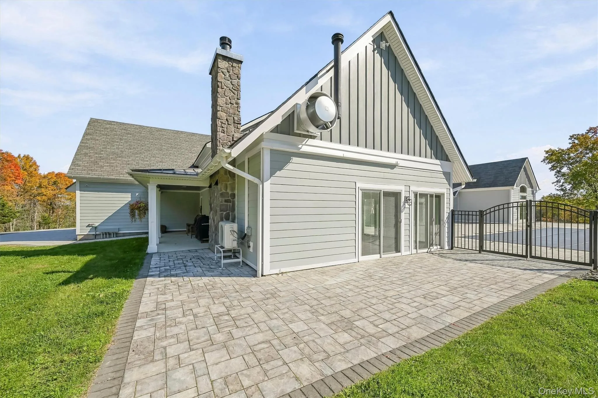 Exterior featuring a stone-clad chimney, composite siding, a paved patio, and a metal perimeter fence around the pool area Exterior featuring a stone-clad chimney, composite siding, a paved patio, and a metal perimeter fence around the pool area