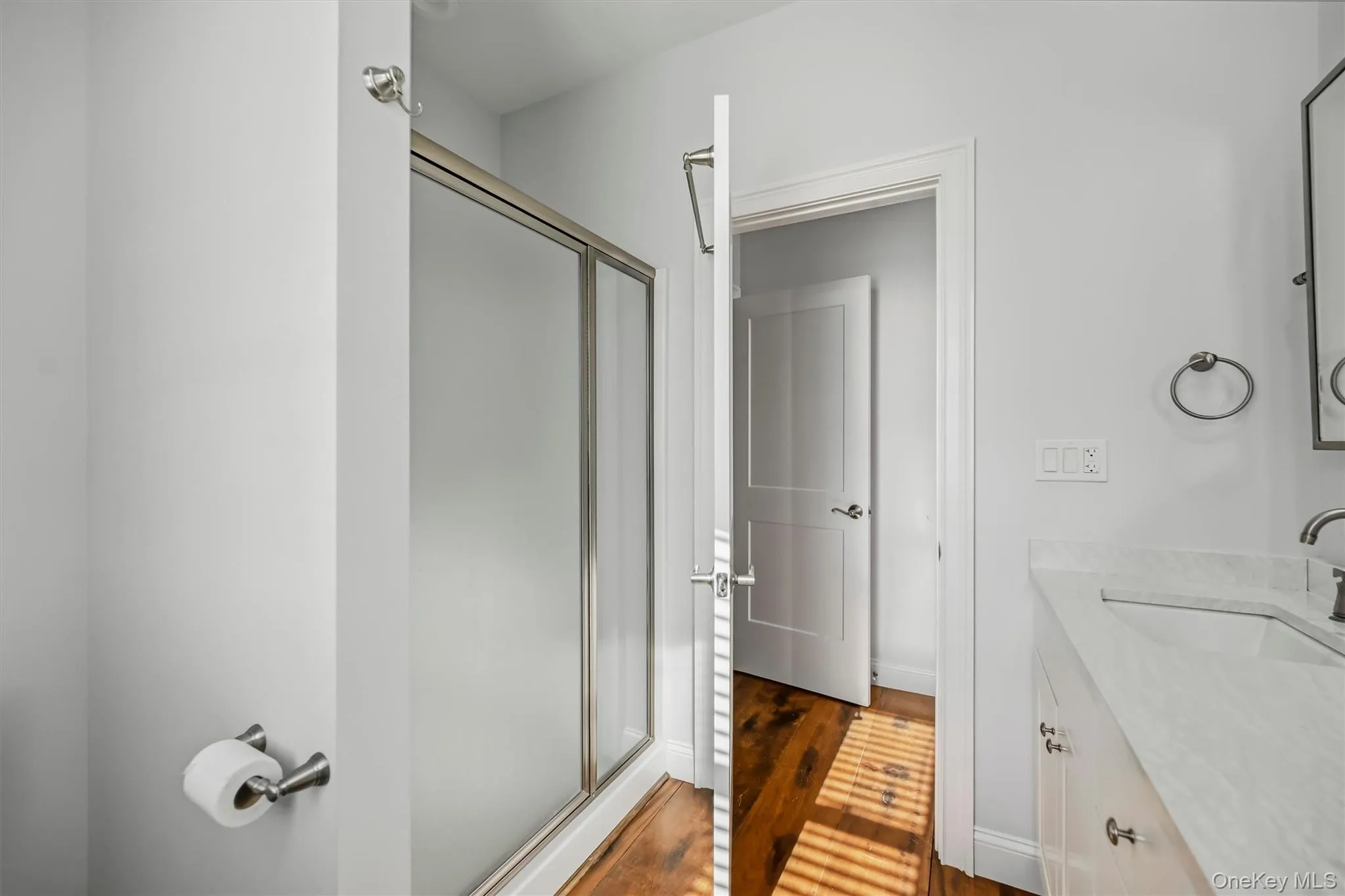 Shower enclosure with a metal frame, vanity featuring a stone countertop with an integrated sink, metal wall-mounted hardware, and wood-finish flooring Shower enclosure with a metal frame, vanity featuring a stone countertop with an integrated sink, metal wall-mounted hardware, and wood-finish flooring