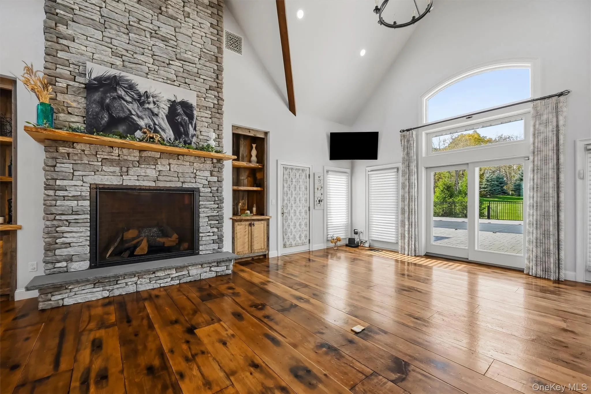 Vaulted ceilings with exposed beams, floor-to-ceiling stone gas fireplace with wood mantel, wood-finish flooring, built-in shelving, and oversized glass sliding doors Vaulted ceilings with exposed beams, floor-to-ceiling stone gas fireplace with wood mantel, wood-finish flooring, built-in shelving, and oversized glass sliding doors