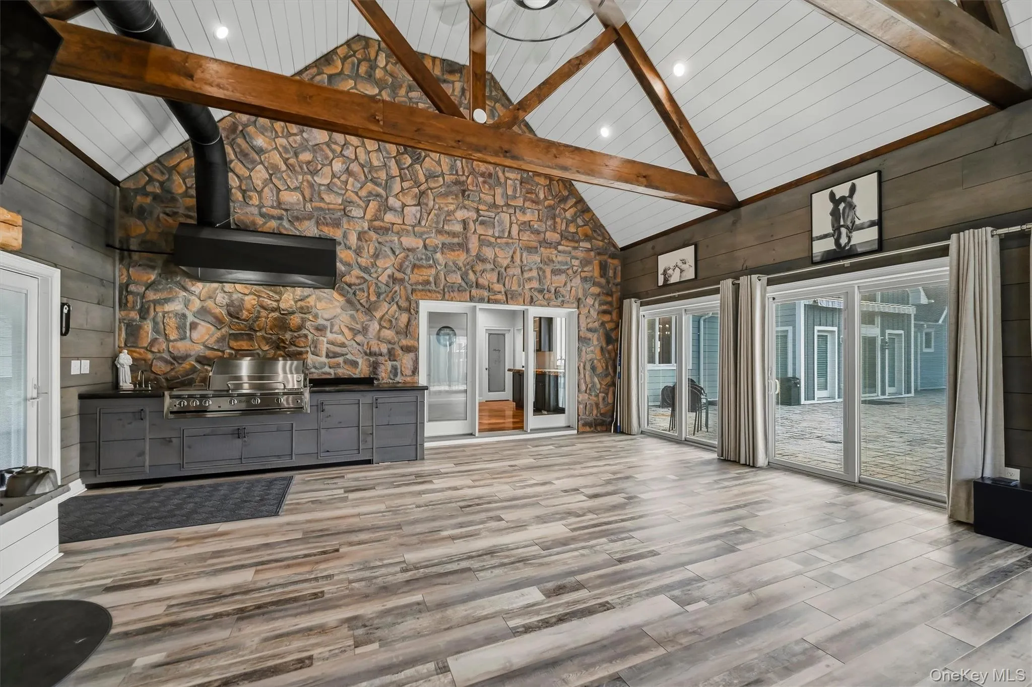 Vaulted ceilings with exposed timber trusses, stone accent wall, wood-finish flooring, built-in cabinetry with stainless steel grill, and glass sliding doors Vaulted ceilings with exposed timber trusses, stone accent wall, wood-finish flooring, built-in cabinetry with stainless steel grill, and glass sliding doors
