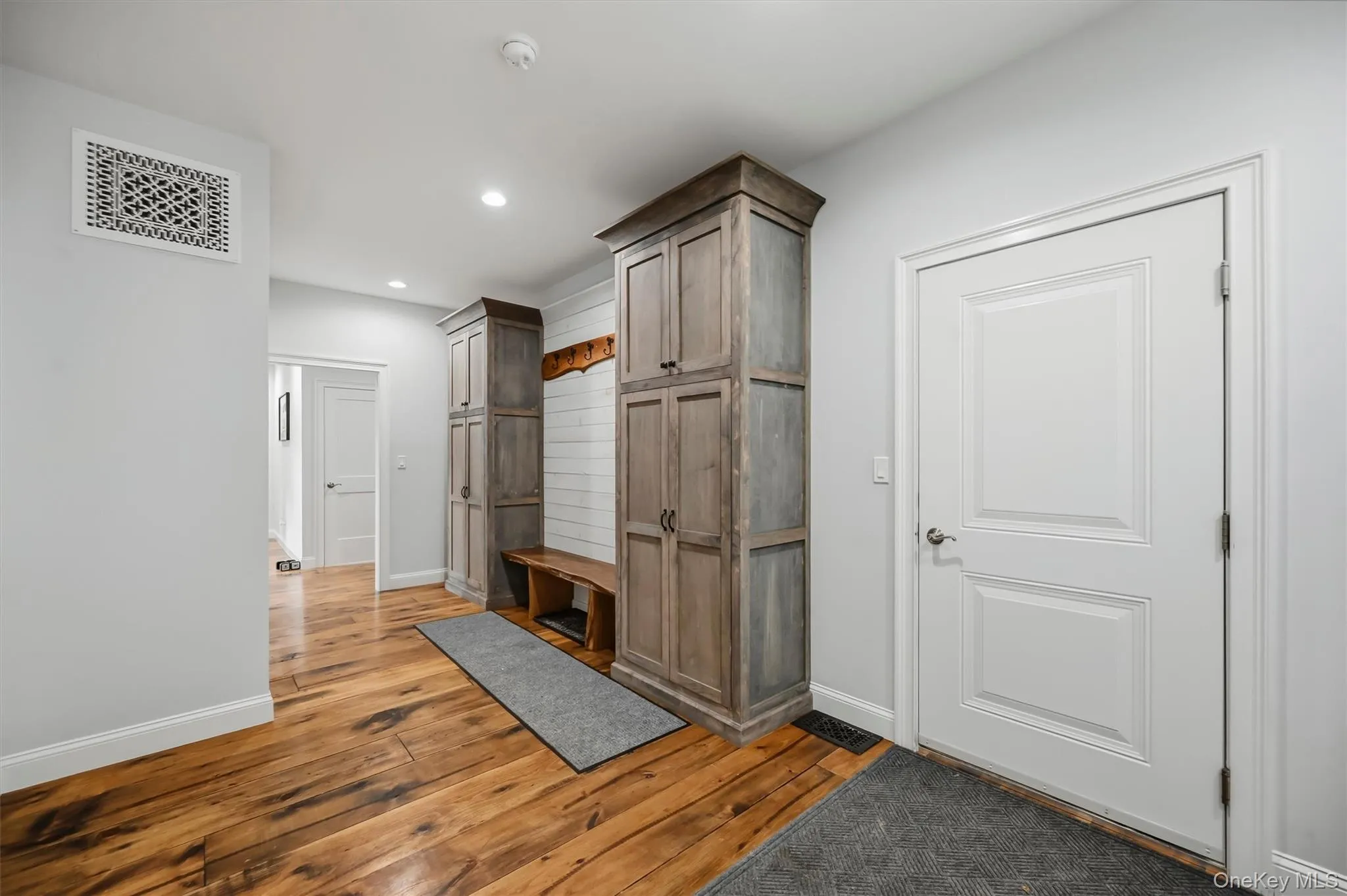 Custom-built cabinetry with wood-finish doors, integrated bench seating, horizontal shiplap wall paneling, and wide-plank wood-finish flooring Custom-built cabinetry with wood-finish doors, integrated bench seating, horizontal shiplap wall paneling, and wide-plank wood-finish flooring