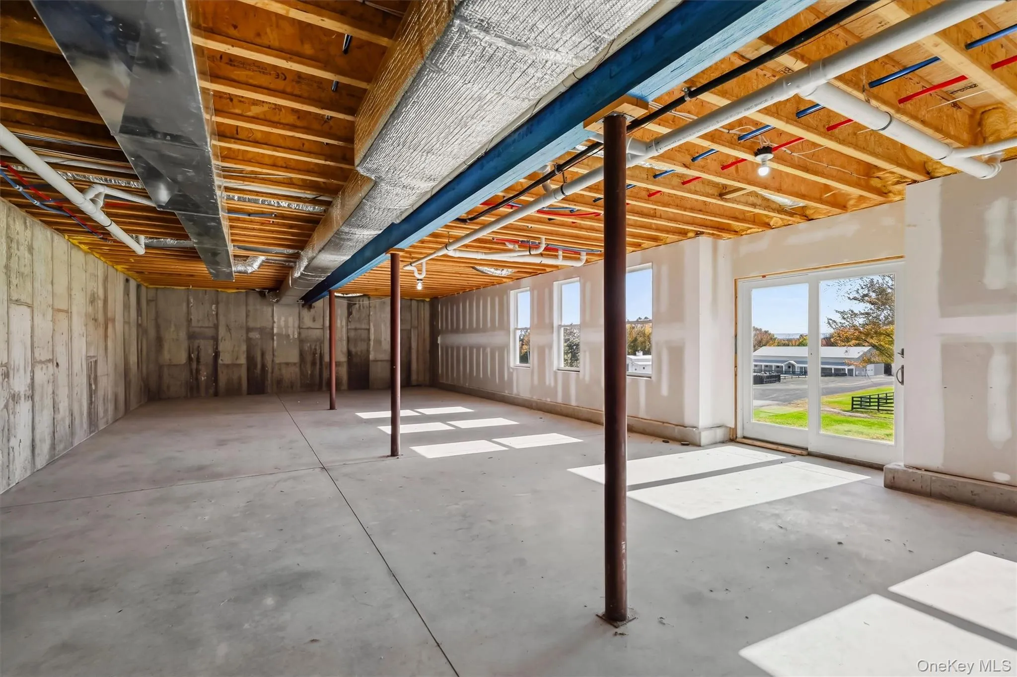 Unfinished space featuring exposed timber joist ceiling, concrete flooring, concrete foundation walls, structural support columns, and sliding glass exterior doors Unfinished space featuring exposed timber joist ceiling, concrete flooring, concrete foundation walls, structural support columns, and sliding glass exterior doors