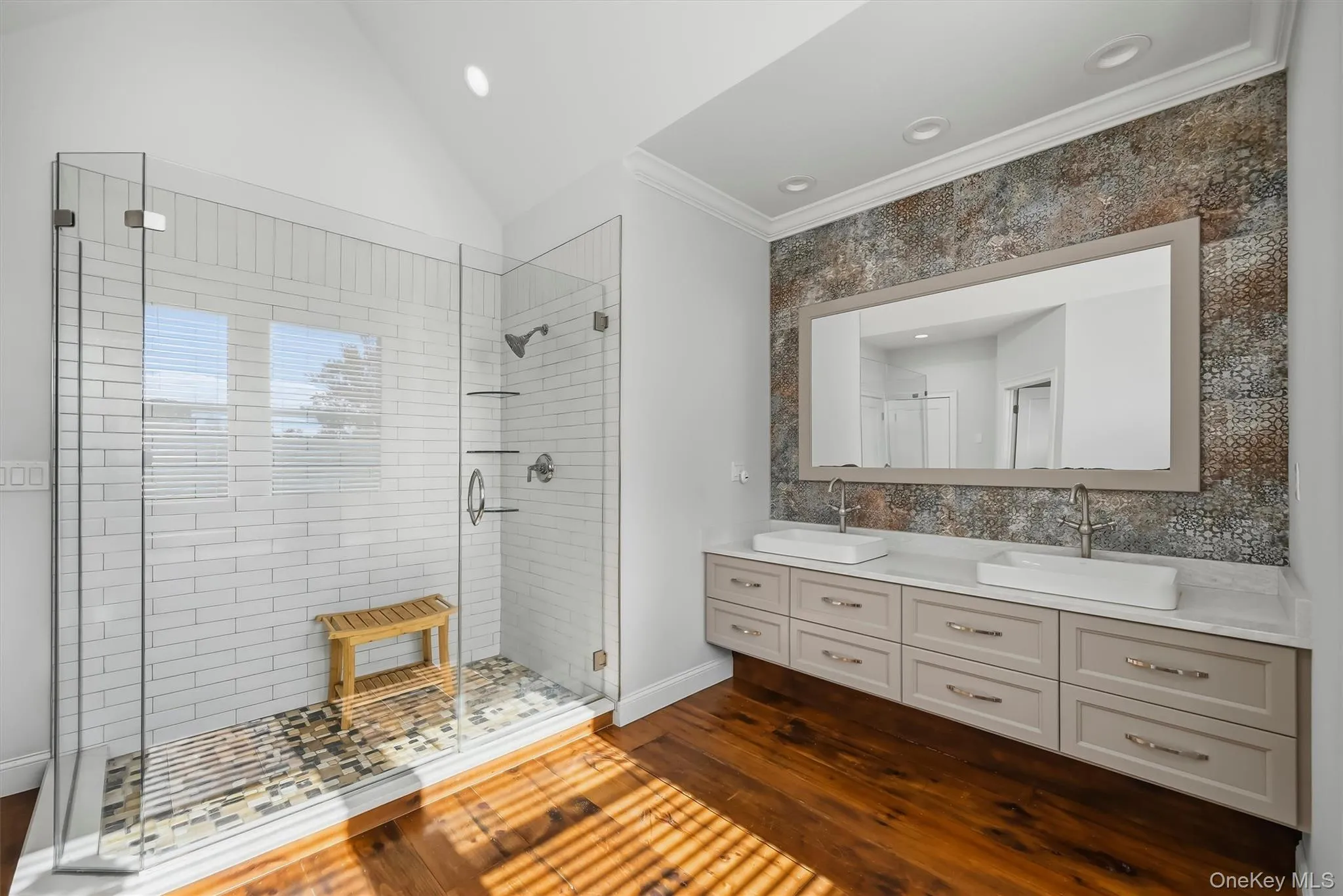 Dual vanity with white vessel sinks and stone countertop, walk-in glass-enclosed shower featuring white subway tile, and wood-finish flooring Dual vanity with white vessel sinks and stone countertop, walk-in glass-enclosed shower featuring white subway tile, and wood-finish flooring