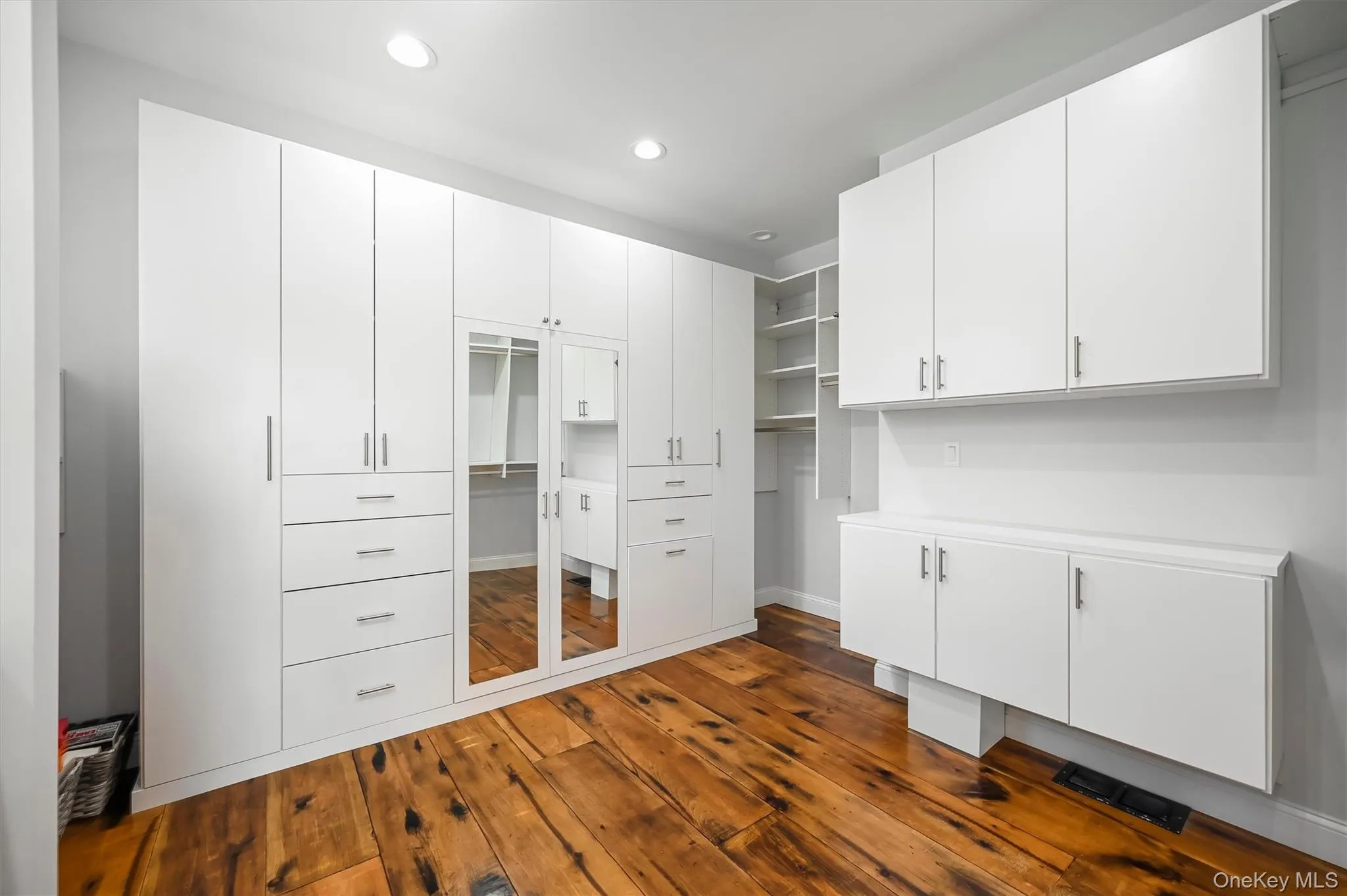 Custom floor-to-ceiling white cabinetry with integrated drawer storage, mirrored paneling, open shelving, and wood-finish flooring Custom floor-to-ceiling white cabinetry with integrated drawer storage, mirrored paneling, open shelving, and wood-finish flooring