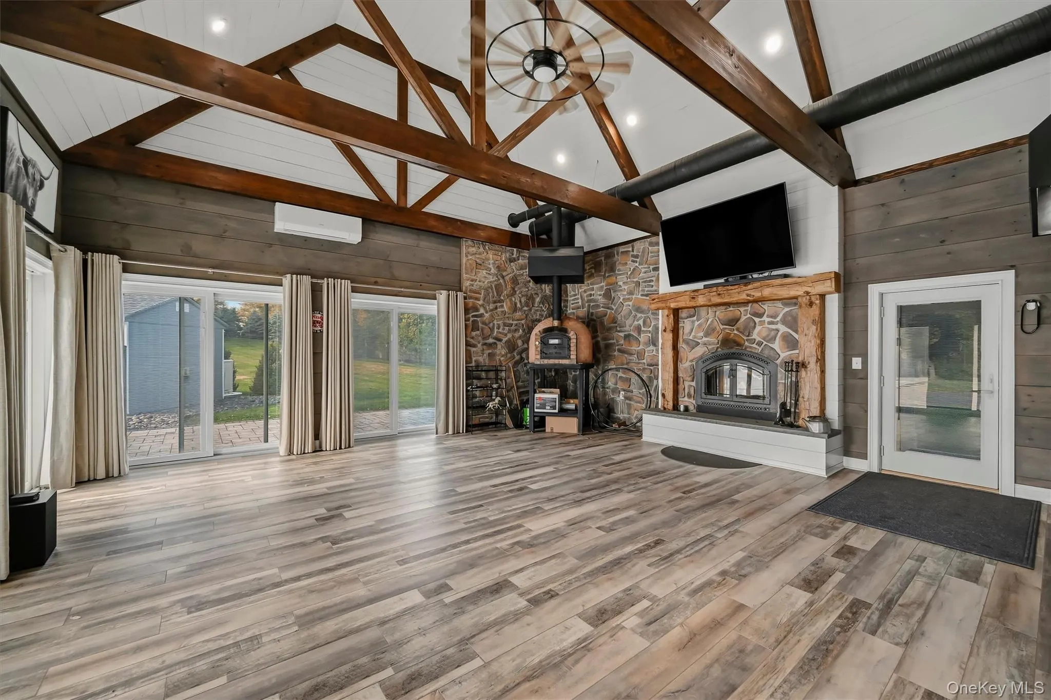 Vaulted ceilings with exposed timber trusses, wood-finish flooring, stone-accentedwood burning fireplace with a timber mantel, integrated stone-clad pizza oven, and multiple sliding glass doors Vaulted ceilings with exposed timber trusses, wood-finish flooring, stone-accentedwood burning fireplace with a timber mantel, integrated stone-clad pizza oven, and multiple sliding glass doors