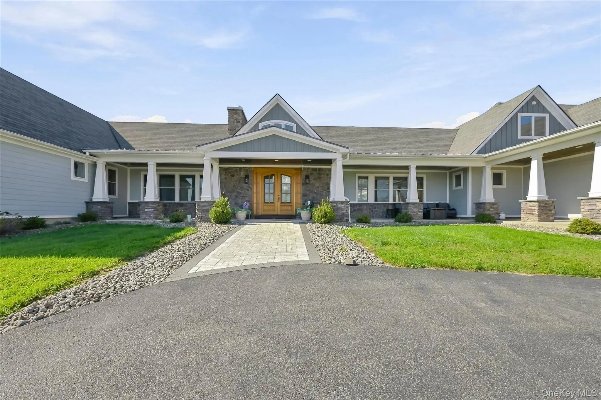 Exterior featuring a horizontal siding facade, stone masonry accents, a covered front porch with white columns, a paved walkway, and double wood-finish entry doors Exterior featuring a horizontal siding facade, stone masonry accents, a covered front porch with white columns, a paved walkway, and double wood-finish entry doors