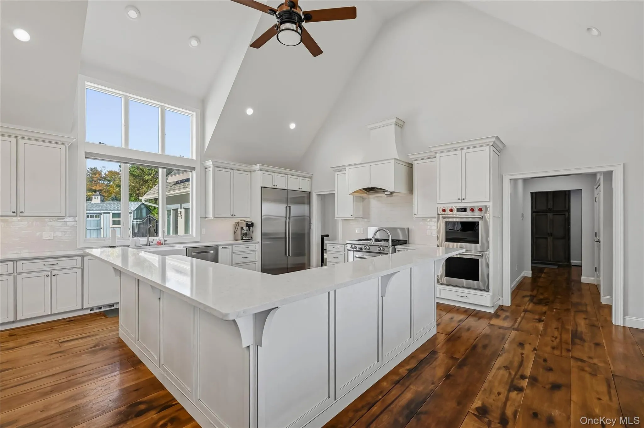 Kitchen featuring vaulted ceilings, wide-plank wood-finish flooring, white shaker-style cabinetry, a quartz surface peninsula, and stainless steel built-in top of the line appliances Kitchen featuring vaulted ceilings, wide-plank wood-finish flooring, white shaker-style cabinetry, a quartz surface peninsula, and stainless steel built-in top of the line appliances
