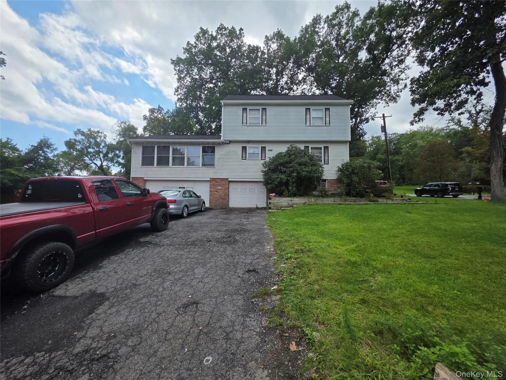 Multi-level exterior featuring light-toned horizontal siding, brick accents, a two-car garage, and expansive yard space Multi-level exterior featuring light-toned horizontal siding, brick accents, a two-car garage, and expansive yard space