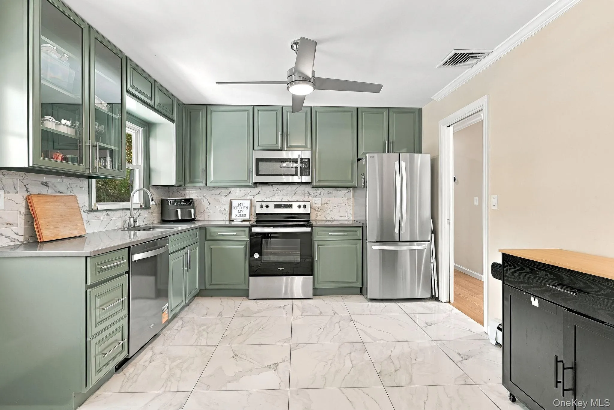 Kitchen featuring sage green cabinetry, stone-finish countertops, stainless steel appliances, marble-patterned tile flooring, and a ceiling fan with integrated lighting Kitchen featuring sage green cabinetry, stone-finish countertops, stainless steel appliances, marble-patterned tile flooring, and a ceiling fan with integrated lighting