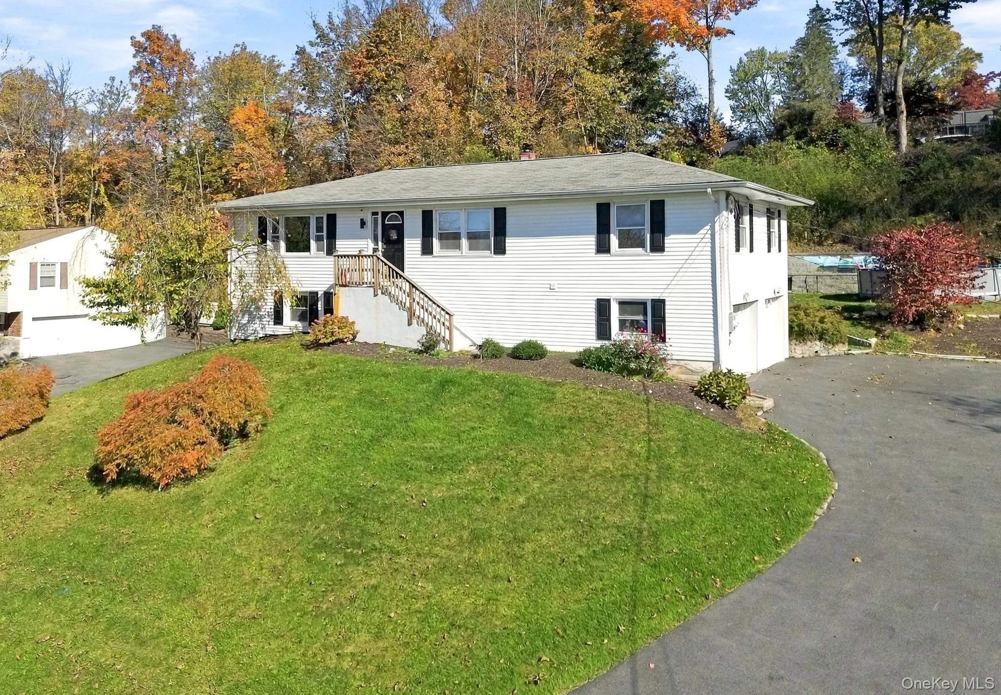 Raised ranch exterior featuring white vinyl siding, black shutters, an elevated wood staircase with railings, and an asphalt driveway Raised ranch exterior featuring white vinyl siding, black shutters, an elevated wood staircase with railings, and an asphalt driveway