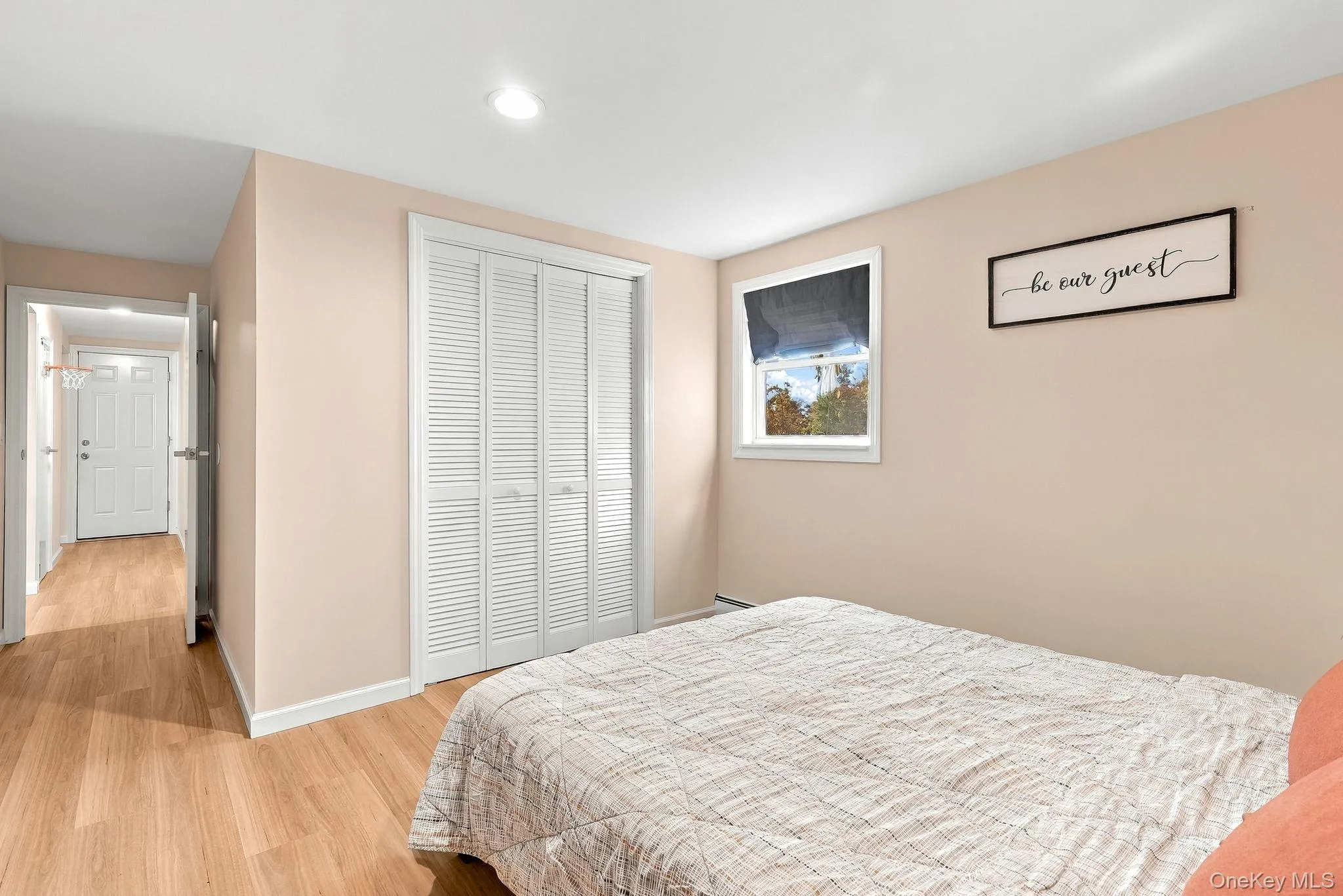 Neutral-toned interior featuring wood-finish flooring, recessed lighting, a single-pane window, and a built-in closet with louvered bifold doors Neutral-toned interior featuring wood-finish flooring, recessed lighting, a single-pane window, and a built-in closet with louvered bifold doors