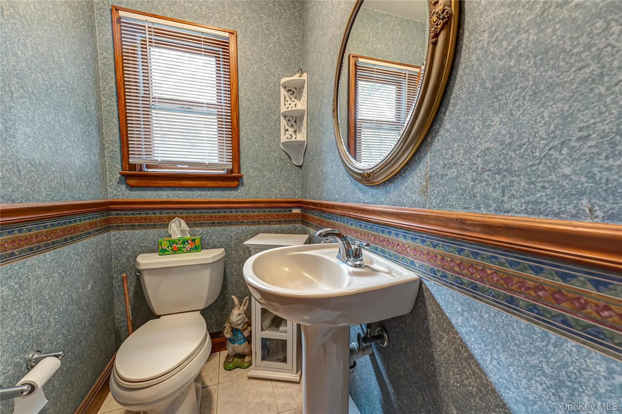 Powder room/half bath with Pedestal sink with chrome faucet, oval wall-mounted mirror, wood-trimmed window. Powder room/half bath with Pedestal sink with chrome faucet, oval wall-mounted mirror, wood-trimmed window.