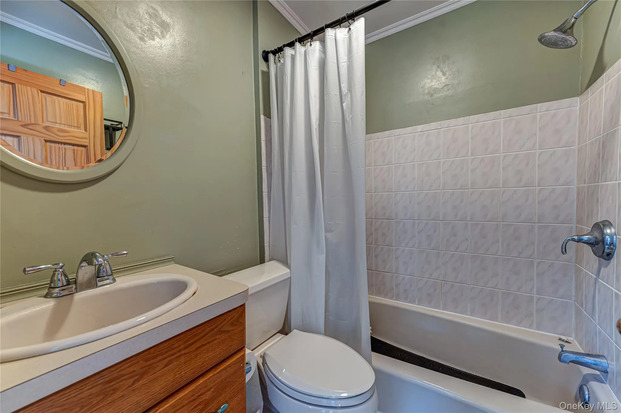 Bathroom featuring a wood-finish vanity, integrated sink, circular wall-mounted mirror, and a tile-surround shower and tub combination Bathroom featuring a wood-finish vanity, integrated sink, circular wall-mounted mirror, and a tile-surround shower and tub combination