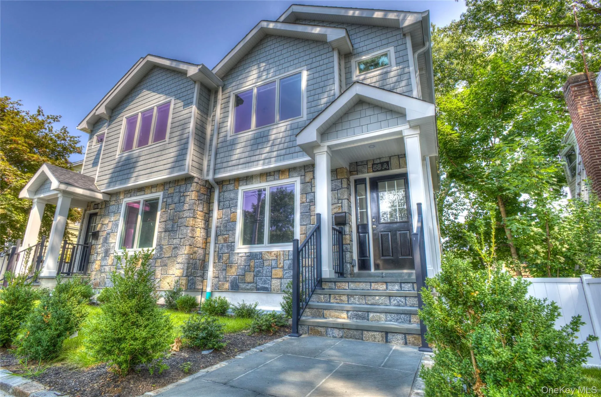 Multi-story exterior featuring stone veneer siding, shingle-style upper cladding, a covered entry with white columns, and a stone-paved walkway Multi-story exterior featuring stone veneer siding, shingle-style upper cladding, a covered entry with white columns, and a stone-paved walkway