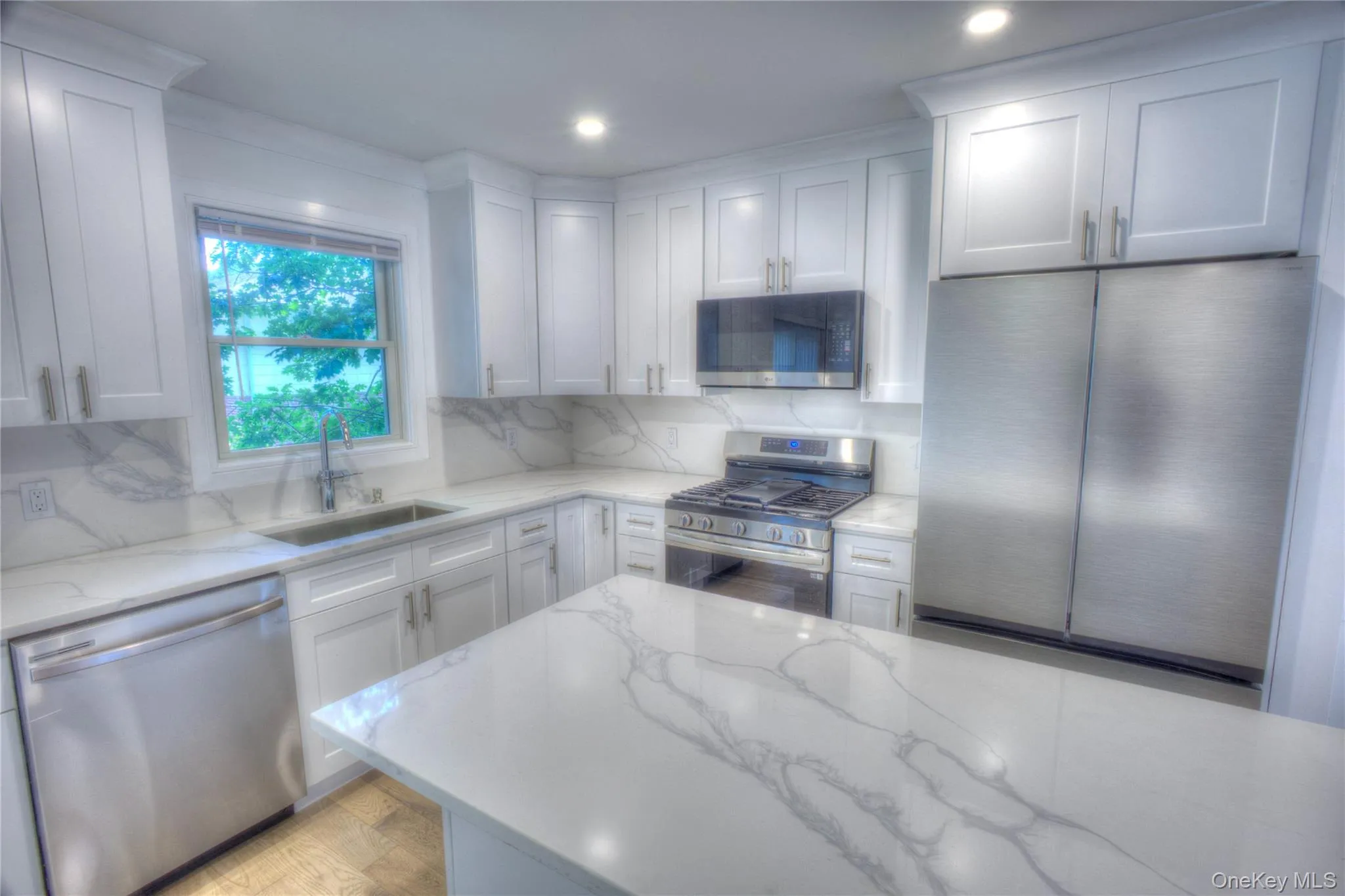 Kitchen featuring white cabinetry, stone-finish countertops with veining, full-height stone-finish backsplash, stainless steel appliances, and a center island Kitchen featuring white cabinetry, stone-finish countertops with veining, full-height stone-finish backsplash, stainless steel appliances, and a center island