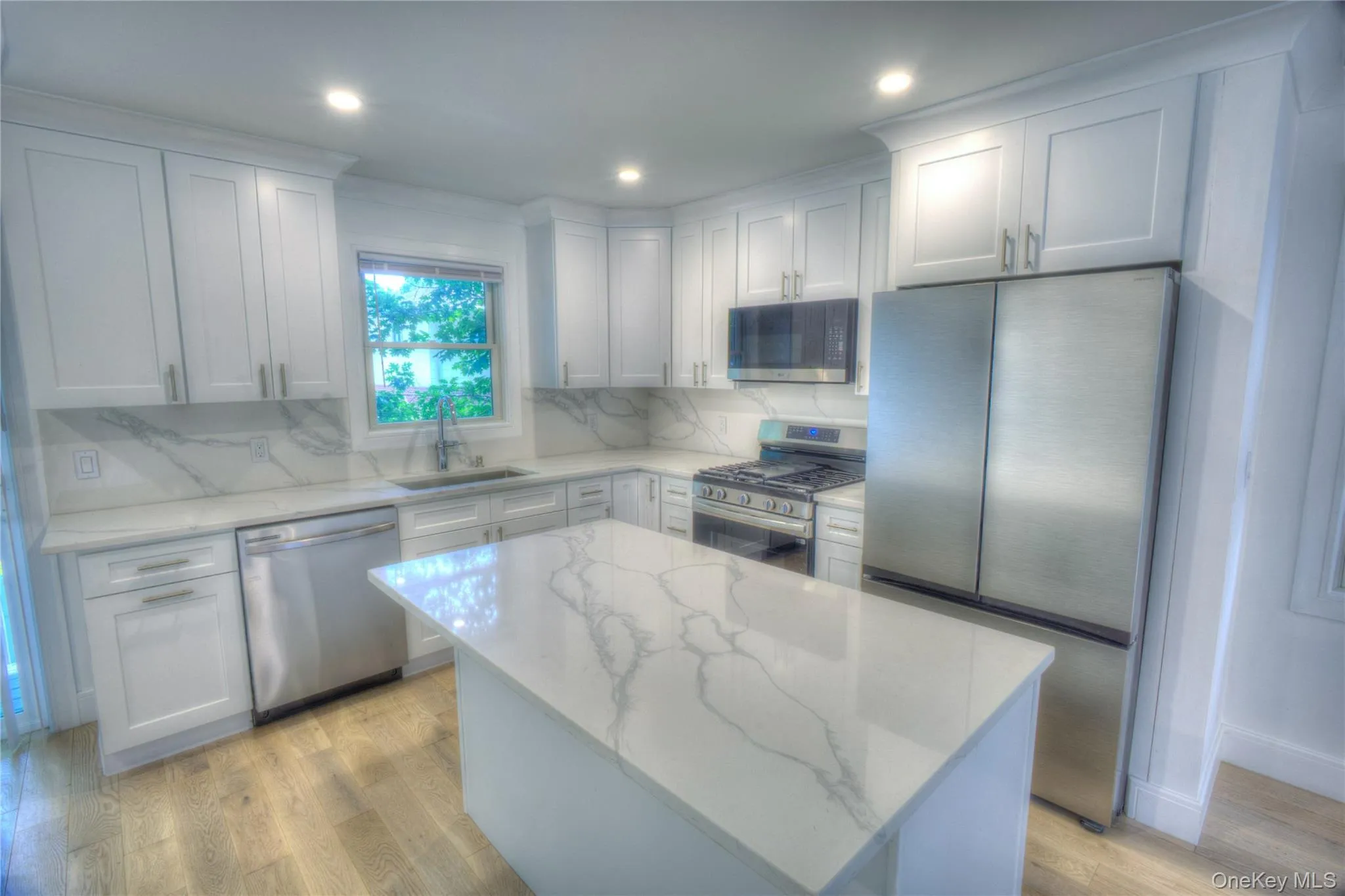 Kitchen featuring white shaker-style cabinetry, stone-patterned countertops, a central island, stainless steel appliances, and wood-finish flooring Kitchen featuring white shaker-style cabinetry, stone-patterned countertops, a central island, stainless steel appliances, and wood-finish flooring