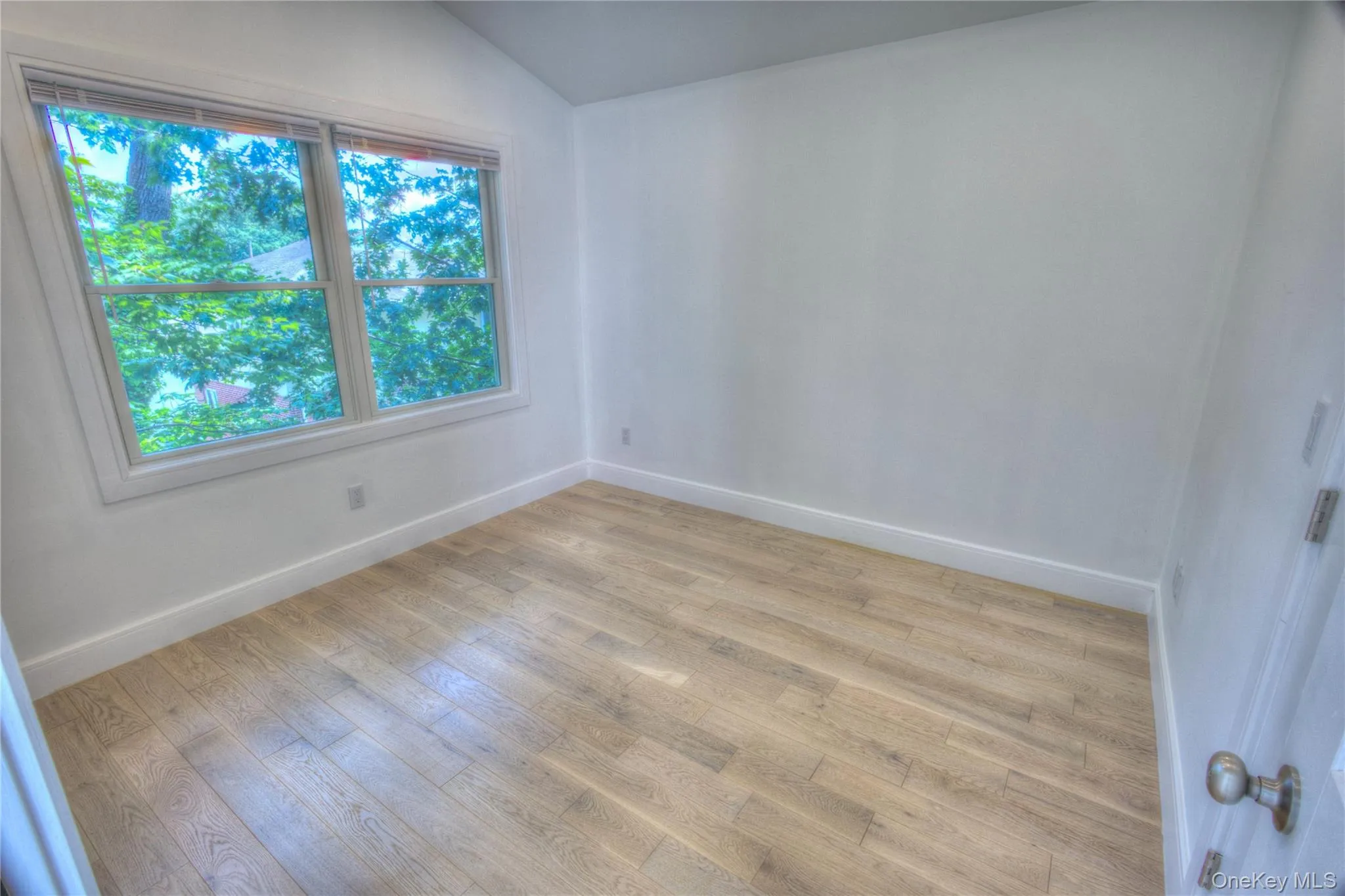 Interior room featuring vaulted ceilings, wood-finish flooring, and a large double-hung window Interior room featuring vaulted ceilings, wood-finish flooring, and a large double-hung window