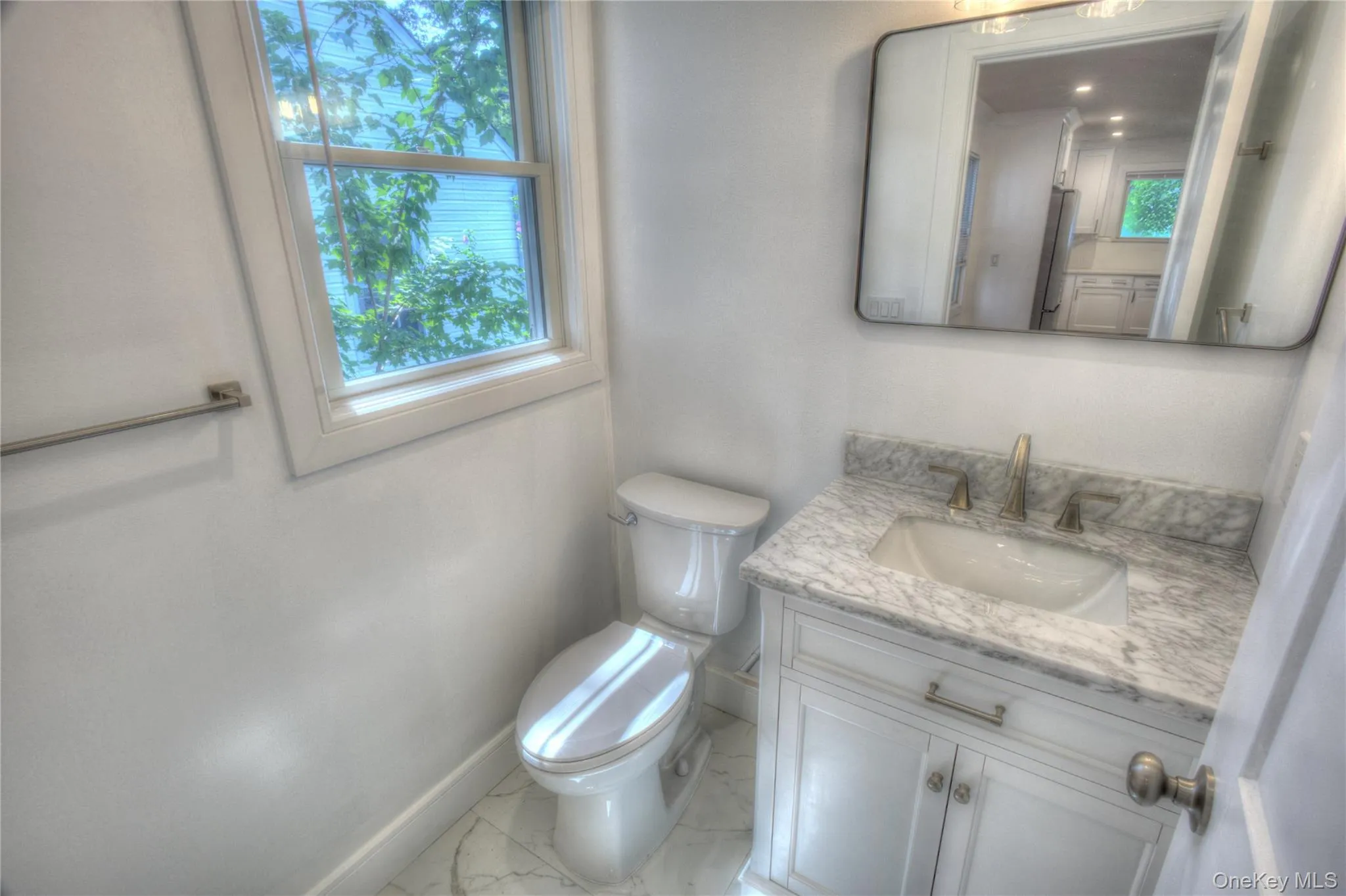 Vanity featuring a stone-patterned countertop, integrated basin with metal hardware, white cabinetry, rectangular wall mirror, and large-format tile flooring Vanity featuring a stone-patterned countertop, integrated basin with metal hardware, white cabinetry, rectangular wall mirror, and large-format tile flooring