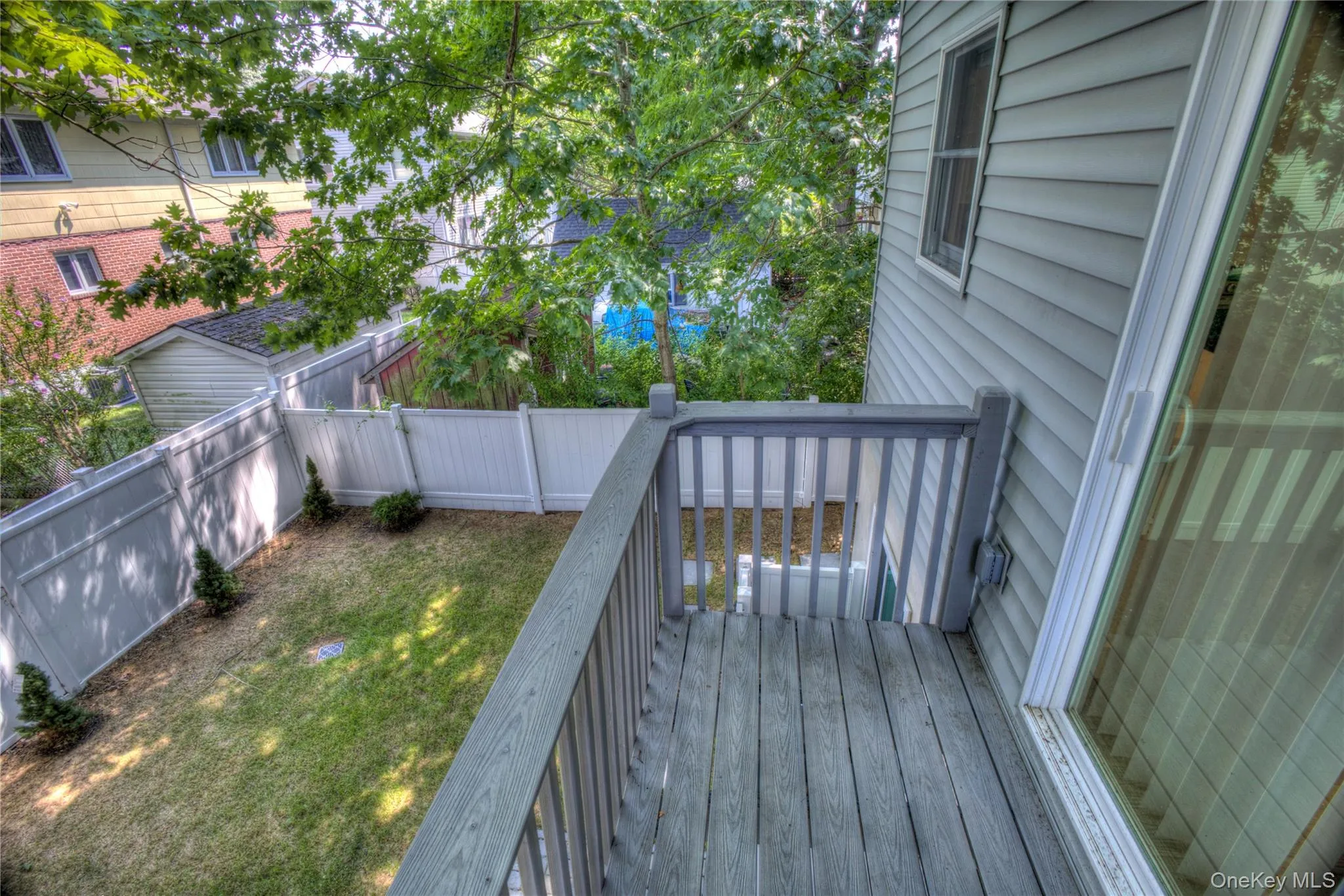 Elevated deck featuring wood-finish decking and vertical railings, overlooking a fenced backyard with a manicured lawn and mature trees Elevated deck featuring wood-finish decking and vertical railings, overlooking a fenced backyard with a manicured lawn and mature trees