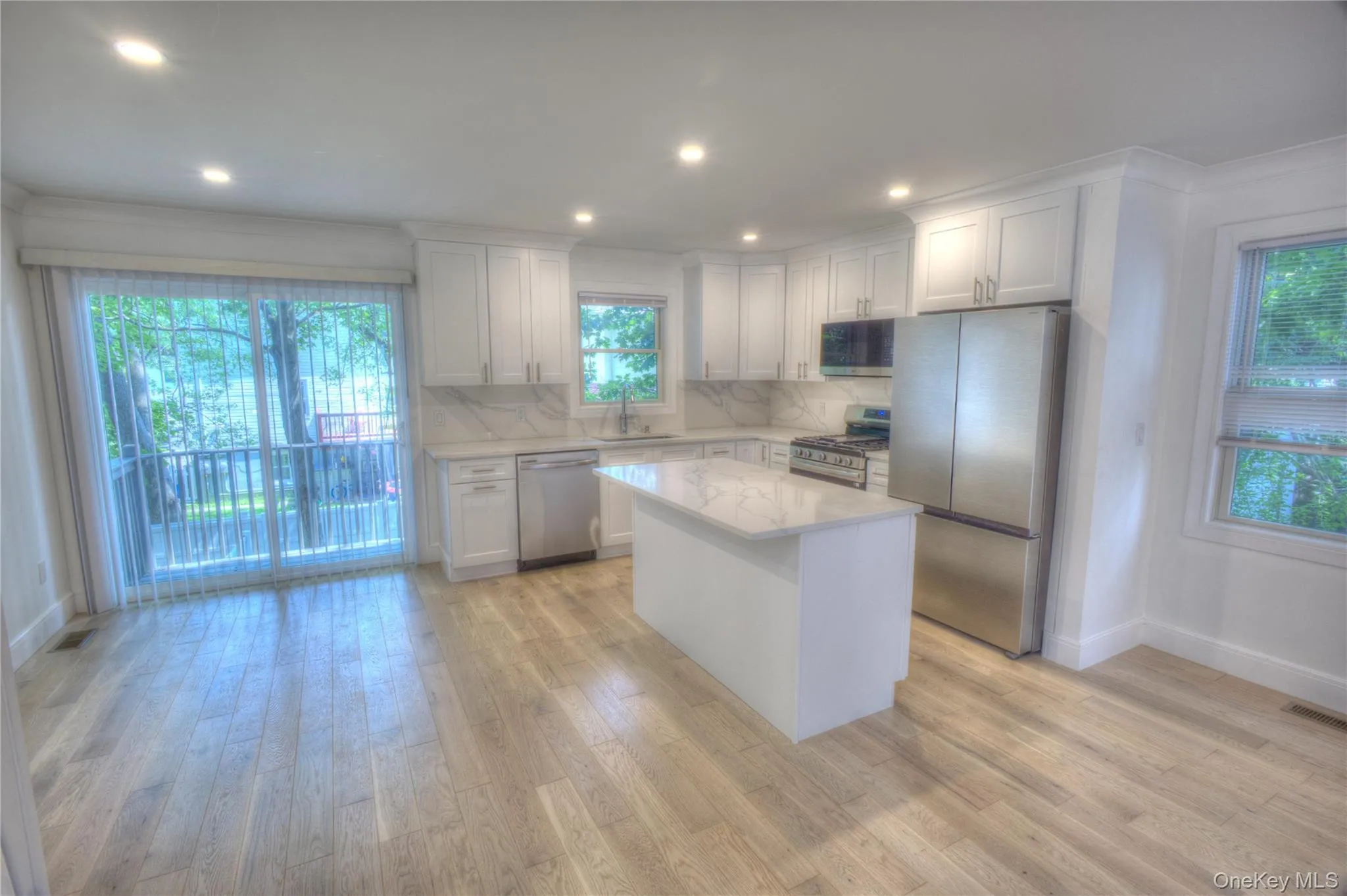 Kitchen featuring shaker-style cabinetry, a central island with a stone-finish countertop, stainless steel appliances, and wood-finish flooring Kitchen featuring shaker-style cabinetry, a central island with a stone-finish countertop, stainless steel appliances, and wood-finish flooring
