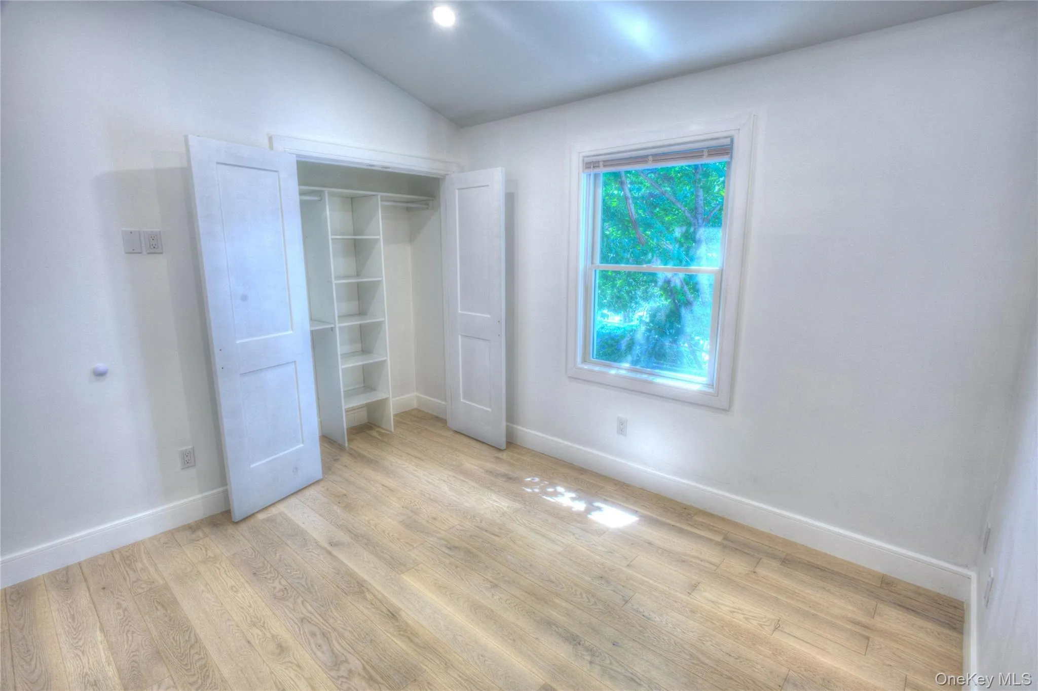 Room featuring wood-finish flooring, recessed lighting, double-hung window, and a reach-in closet with built-in shelving Room featuring wood-finish flooring, recessed lighting, double-hung window, and a reach-in closet with built-in shelving