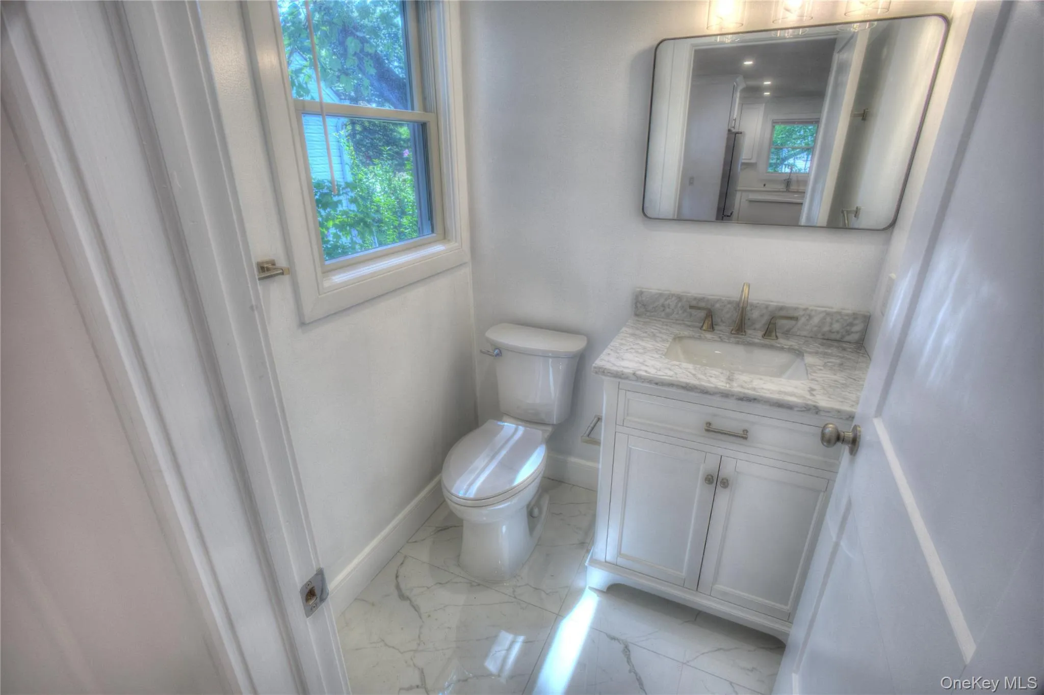 White cabinetry vanity with stone-composite countertop, undermount sink, metallic faucet, rectangular wall-mounted mirror, and stone-patterned tile flooring White cabinetry vanity with stone-composite countertop, undermount sink, metallic faucet, rectangular wall-mounted mirror, and stone-patterned tile flooring