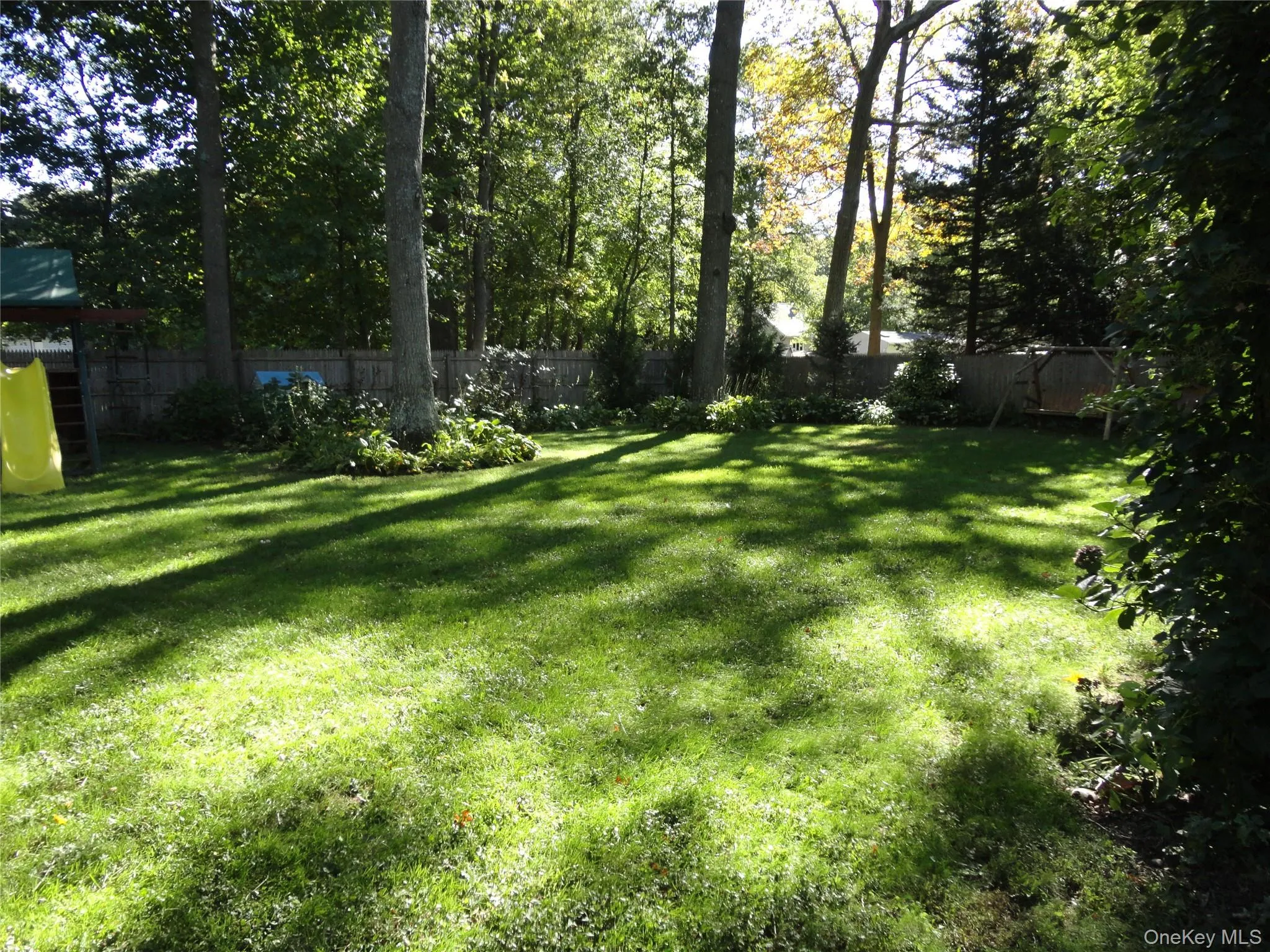 Backyard featuring a level lawn, mature trees, wood privacy fencing, and landscaping beds Backyard featuring a level lawn, mature trees, wood privacy fencing, and landscaping beds