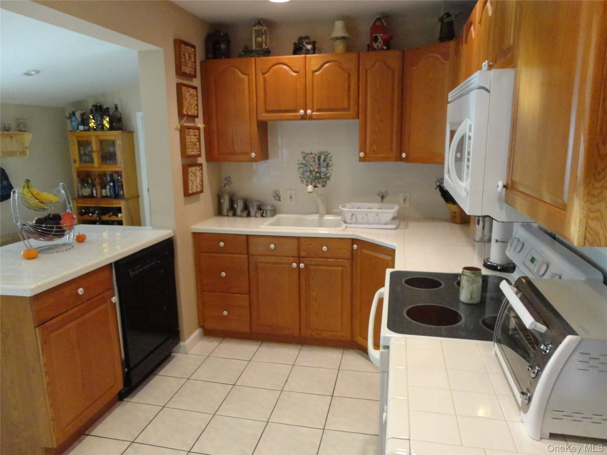 Kitchen featuring wood cabinetry, white tile countertops, tile flooring, and a built-in electric range with over-the-range microwave Kitchen featuring wood cabinetry, white tile countertops, tile flooring, and a built-in electric range with over-the-range microwave