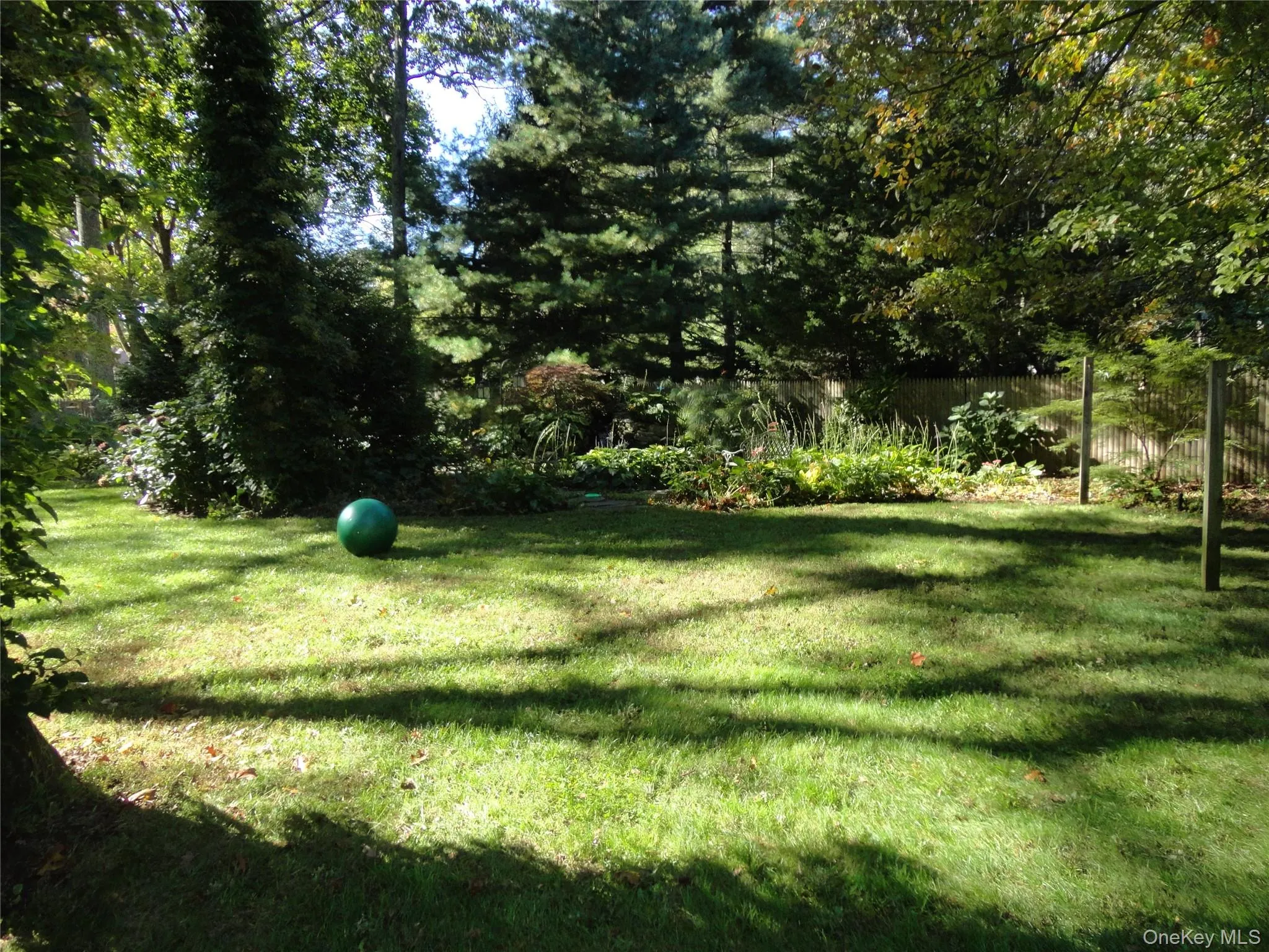 Expansive backyard featuring a lush grass lawn, mature trees, ornamental garden beds, and a perimeter privacy fence Expansive backyard featuring a lush grass lawn, mature trees, ornamental garden beds, and a perimeter privacy fence