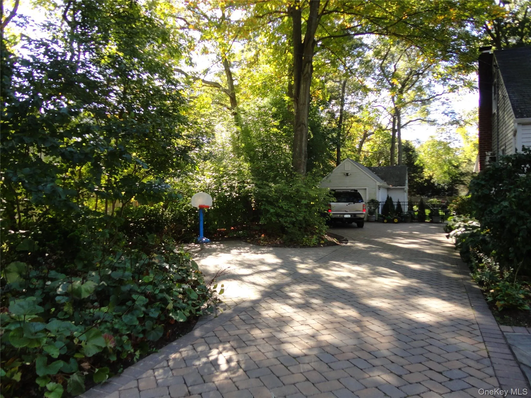 Paver driveway featuring a detached garage and mature perimeter landscaping Paver driveway featuring a detached garage and mature perimeter landscaping