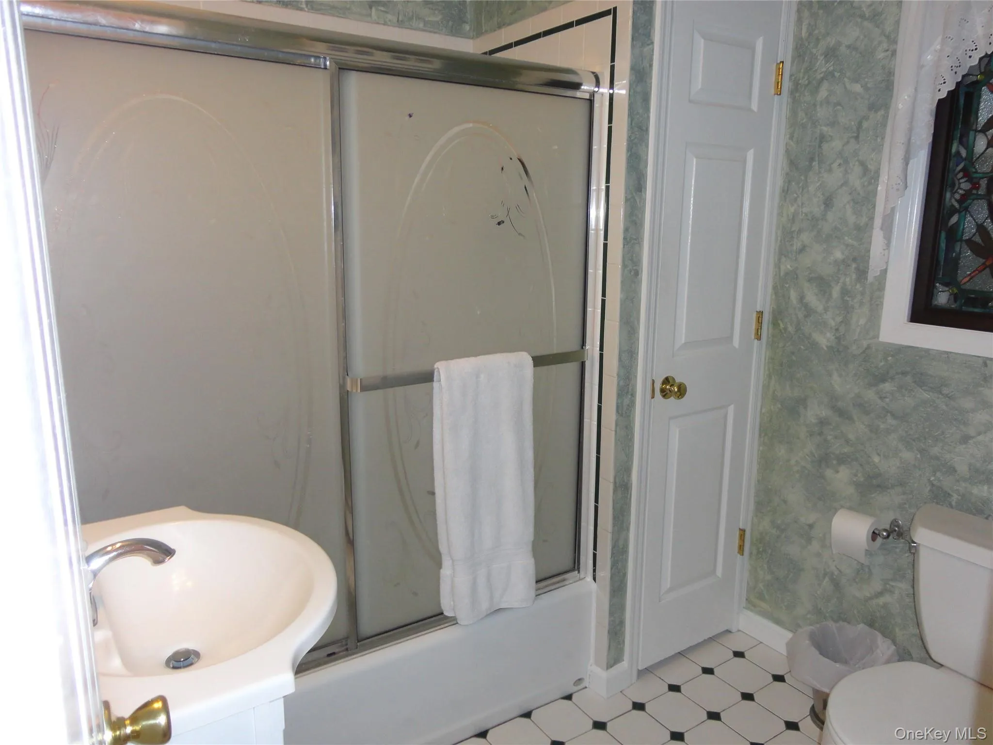 Pedestal sink with a polished chrome faucet, sliding glass shower door enclosure, and checkered tile flooring Pedestal sink with a polished chrome faucet, sliding glass shower door enclosure, and checkered tile flooring