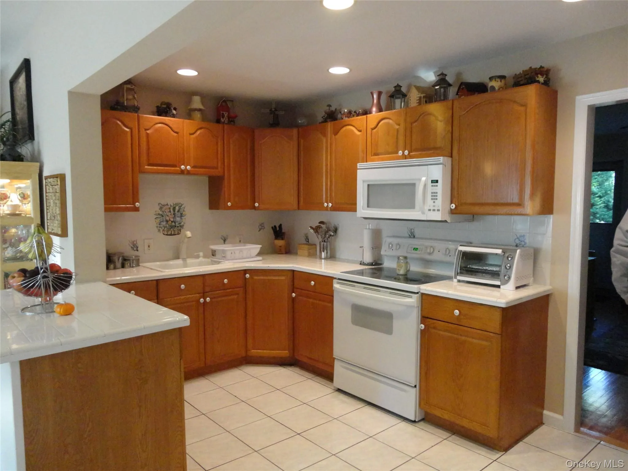 Kitchen featuring wood cabinetry, white countertops, tile backsplash, tile flooring, and recessed ceiling lighting Kitchen featuring wood cabinetry, white countertops, tile backsplash, tile flooring, and recessed ceiling lighting