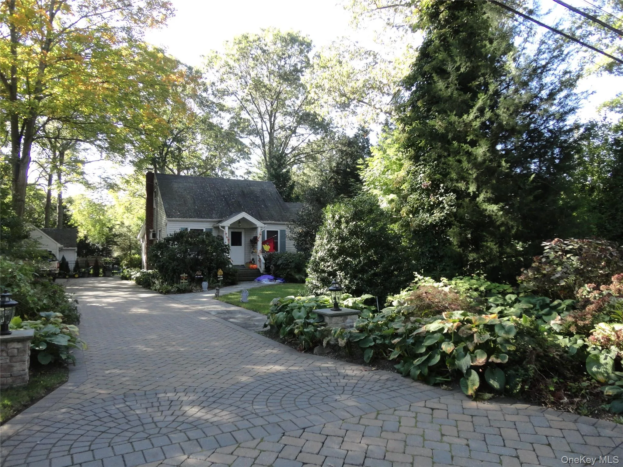 Exterior featuring a paved driveway with circular pattern detailing, mature landscaping, and a covered front entry Exterior featuring a paved driveway with circular pattern detailing, mature landscaping, and a covered front entry