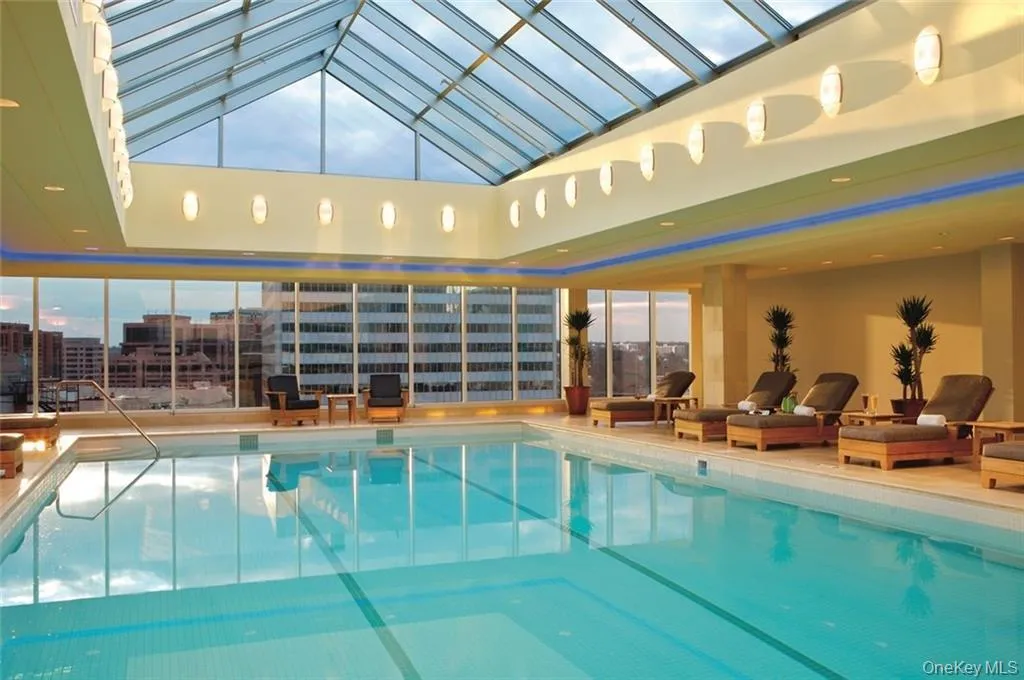 Pool featuring a view of city, glass enclosure, and a patio area Pool featuring a view of city, glass enclosure, and a patio area