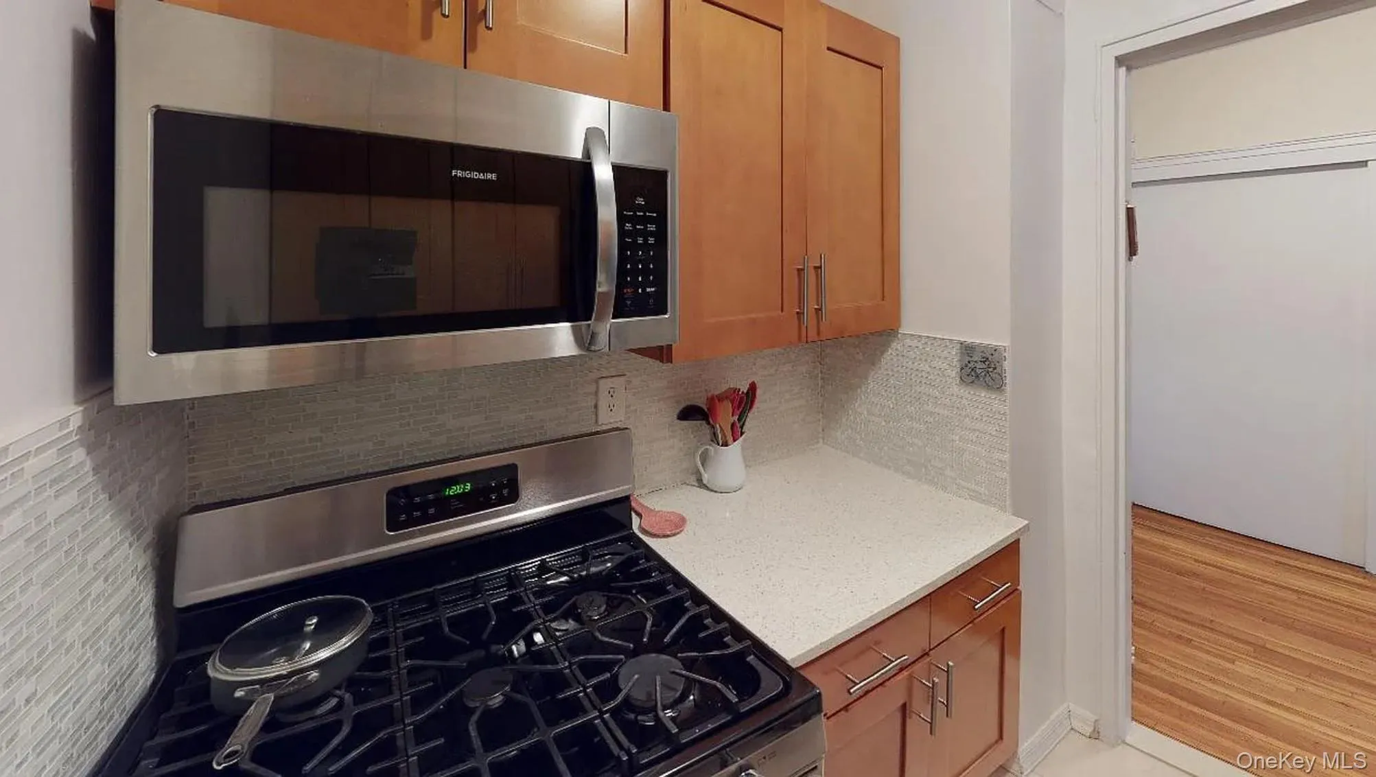 Kitchen featuring stainless steel appliances including a gas range and built-in microwave, wood-finish cabinetry, stone-texture countertop, and a tiled backsplash Kitchen featuring stainless steel appliances including a gas range and built-in microwave, wood-finish cabinetry, stone-texture countertop, and a tiled backsplash