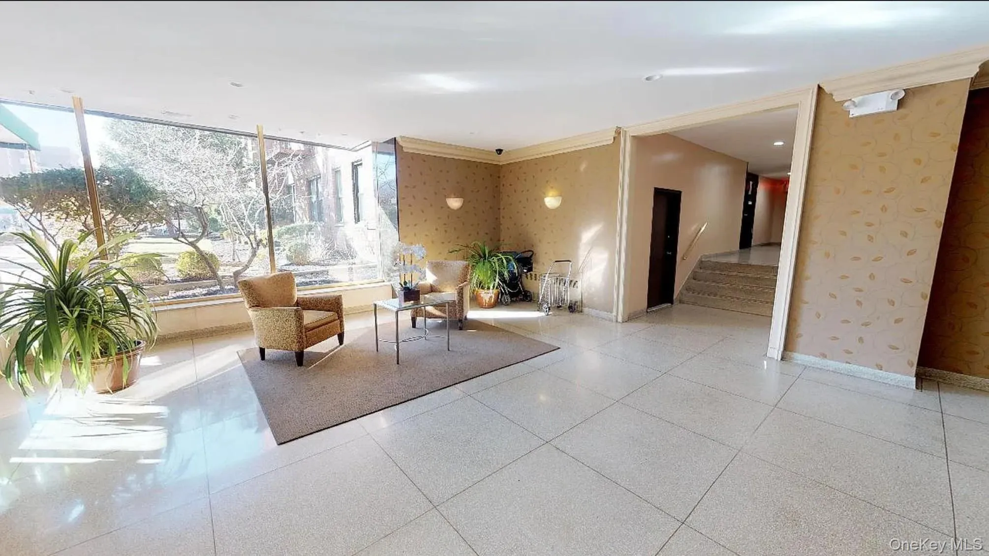 Lobby featuring floor-to-ceiling windows, large-format tile flooring, patterned wallpaper, and wall-mounted sconce lighting Lobby featuring floor-to-ceiling windows, large-format tile flooring, patterned wallpaper, and wall-mounted sconce lighting