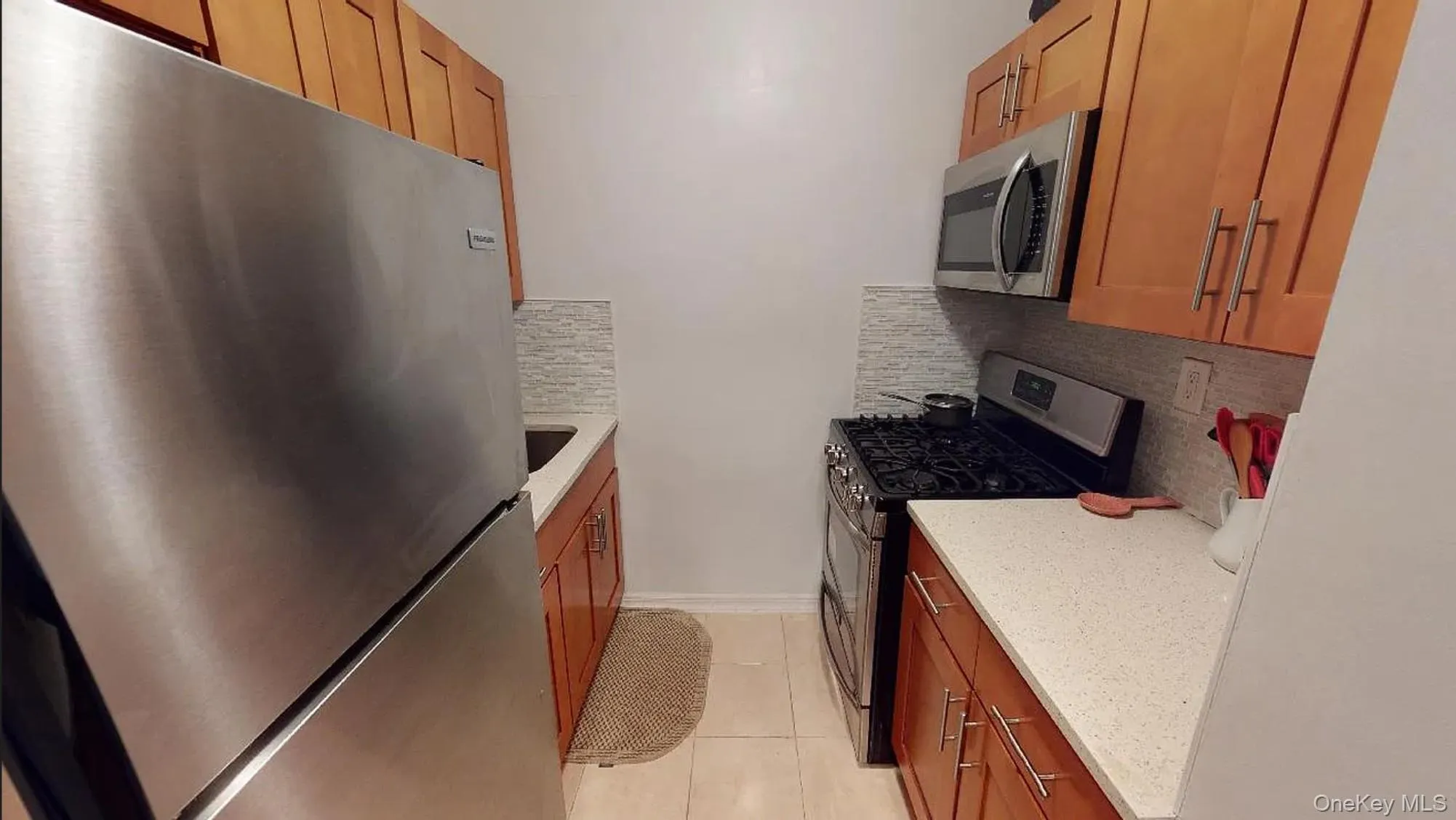 Kitchen featuring stainless steel appliances, light-toned cabinetry, light-colored stone-finish countertops, tile backsplash, and tile flooring Kitchen featuring stainless steel appliances, light-toned cabinetry, light-colored stone-finish countertops, tile backsplash, and tile flooring