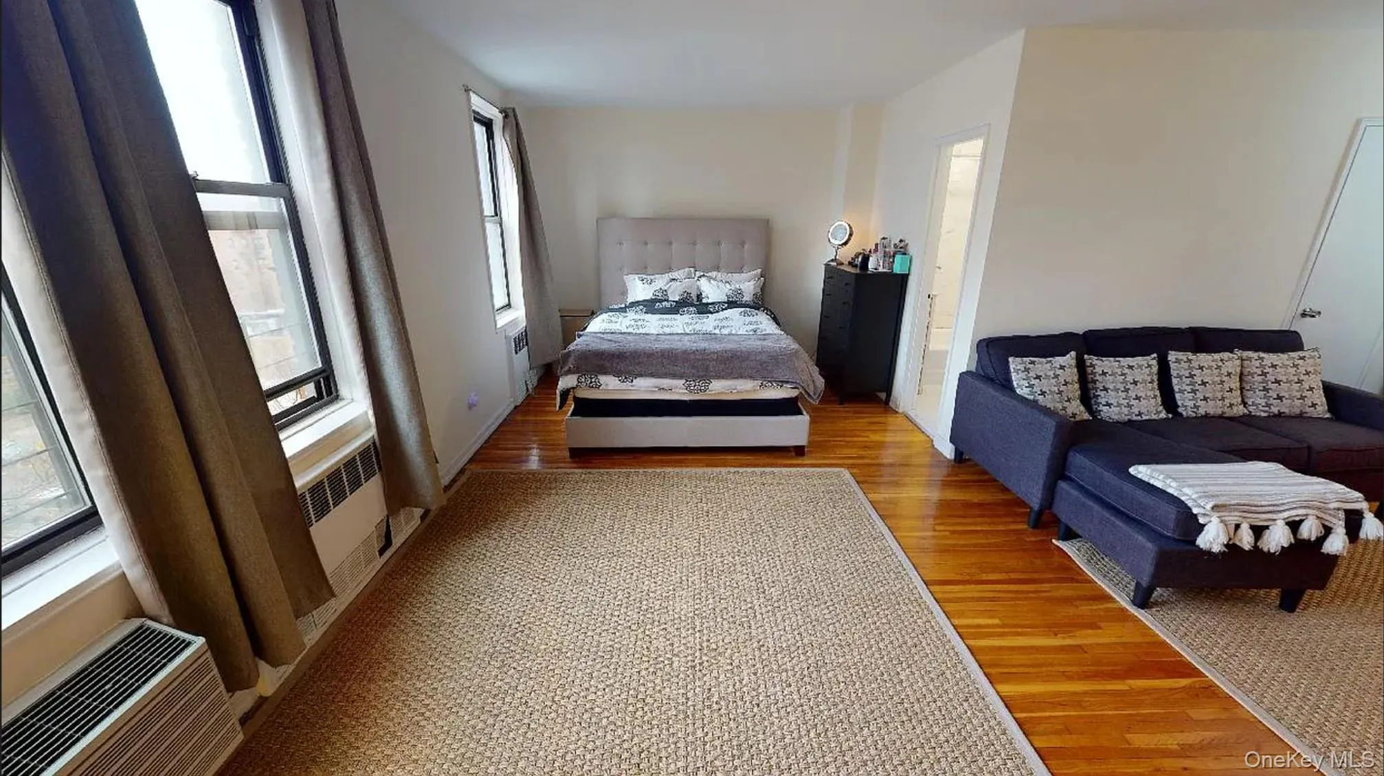 Open-concept room featuring wood-finish flooring, dual windows, and an integrated heating and cooling unit Open-concept room featuring wood-finish flooring, dual windows, and an integrated heating and cooling unit