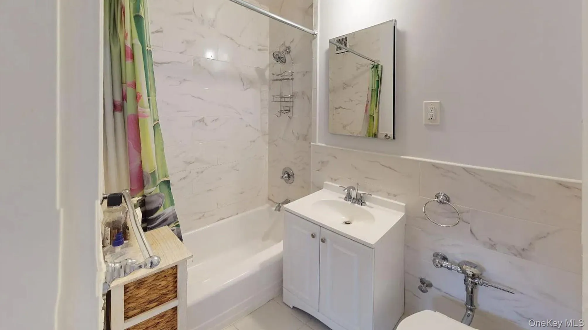 Bathroom featuring stone-finish wall tile, white vanity cabinet with integrated sink, rectangular wall-mounted mirror, and chrome fixtures Bathroom featuring stone-finish wall tile, white vanity cabinet with integrated sink, rectangular wall-mounted mirror, and chrome fixtures
