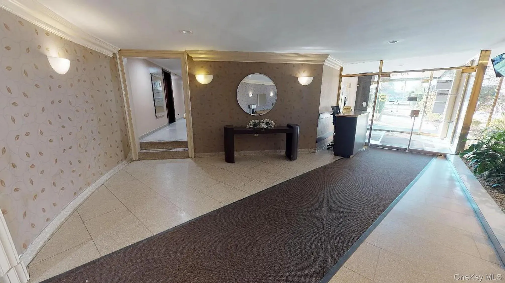 Foyer featuring large-format tile flooring, patterned wall coverings, integrated wall-mounted sconces, and an expansive glass-paneled entrance with metal framing Foyer featuring large-format tile flooring, patterned wall coverings, integrated wall-mounted sconces, and an expansive glass-paneled entrance with metal framing