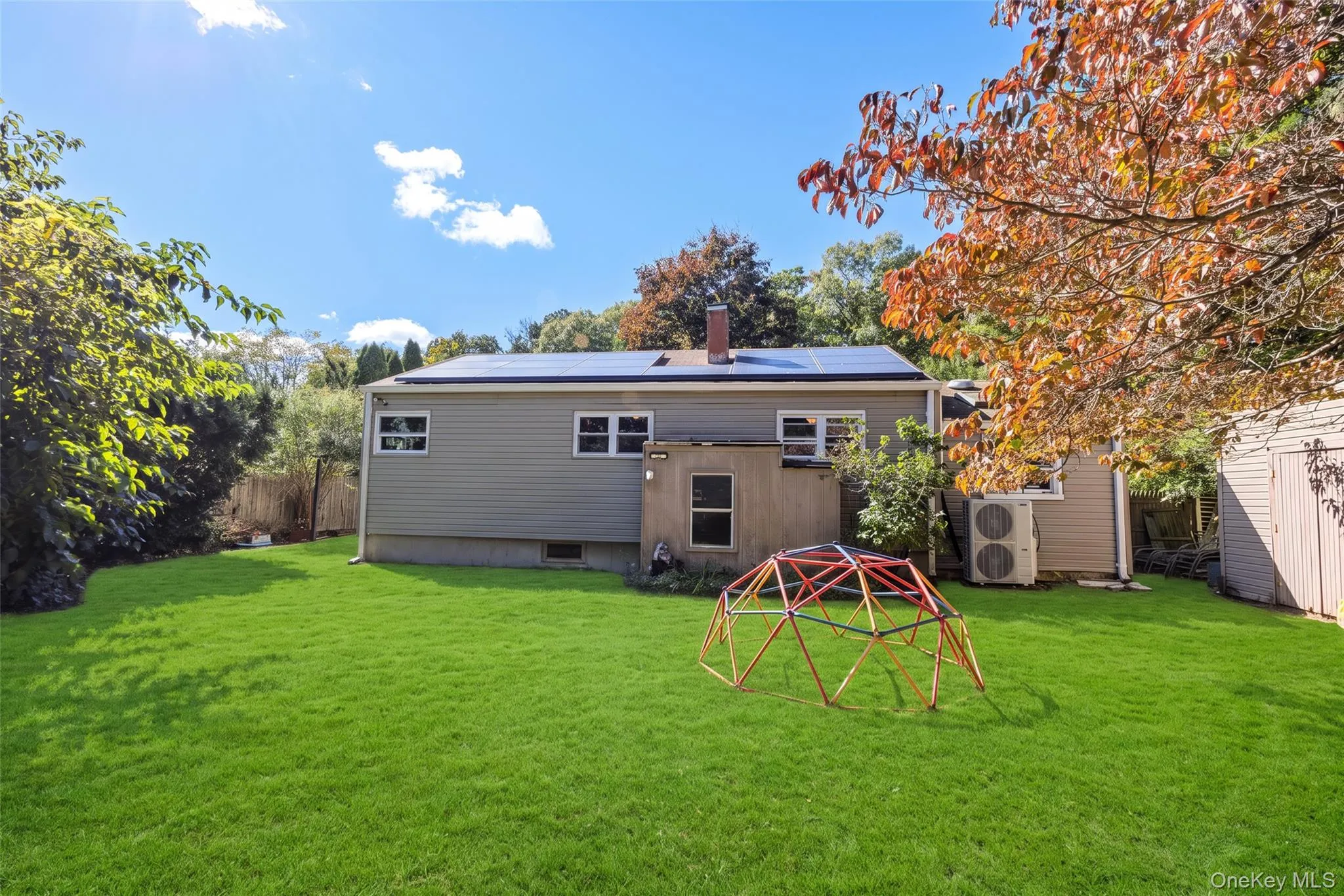 Rear exterior featuring horizontal vinyl siding, roof-mounted solar panels, a brick chimney, and an expansive lawn Rear exterior featuring horizontal vinyl siding, roof-mounted solar panels, a brick chimney, and an expansive lawn