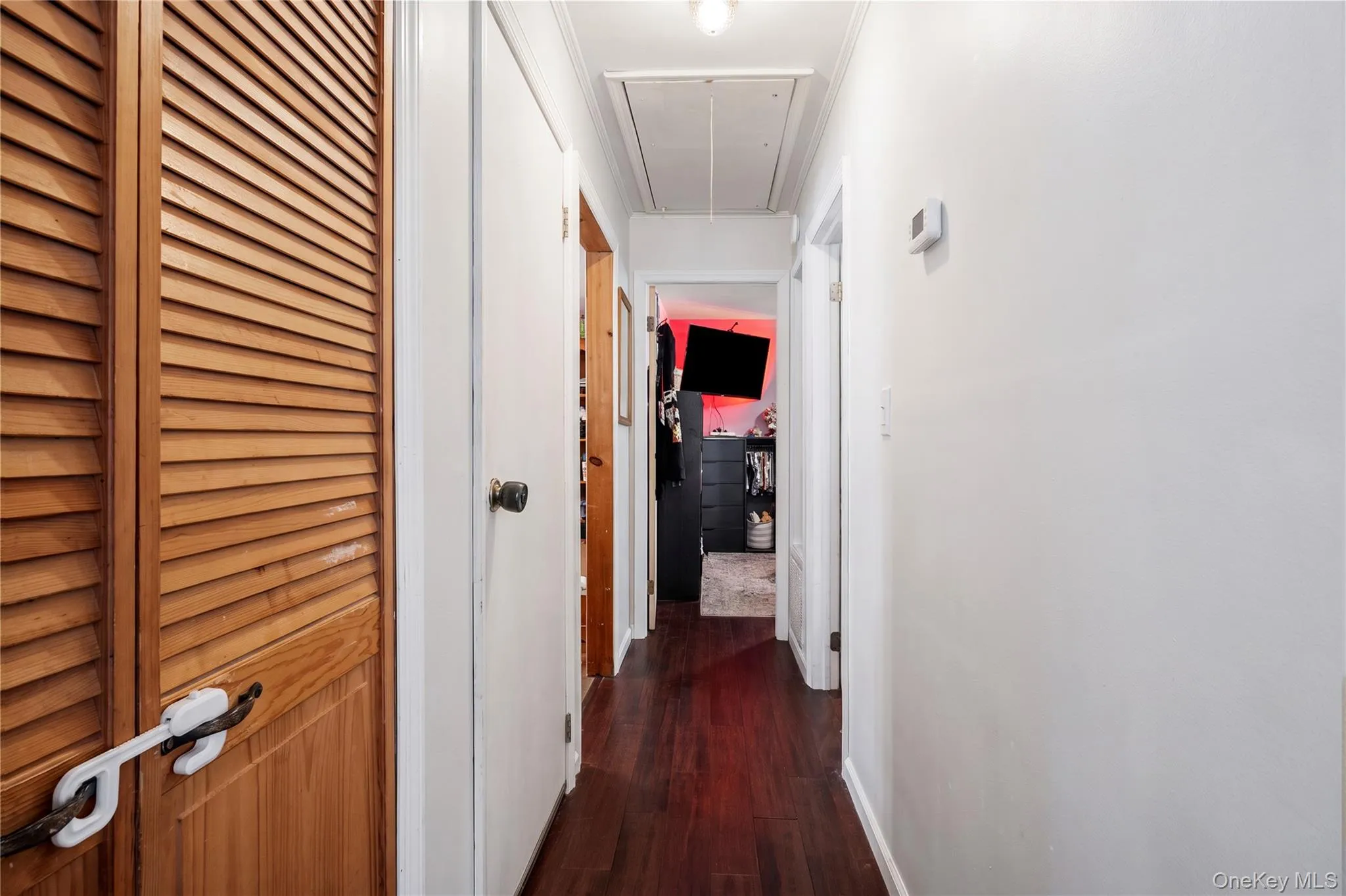 Hallway featuring wood-finish flooring, louvered wood closet doors, and recessed attic access Hallway featuring wood-finish flooring, louvered wood closet doors, and recessed attic access