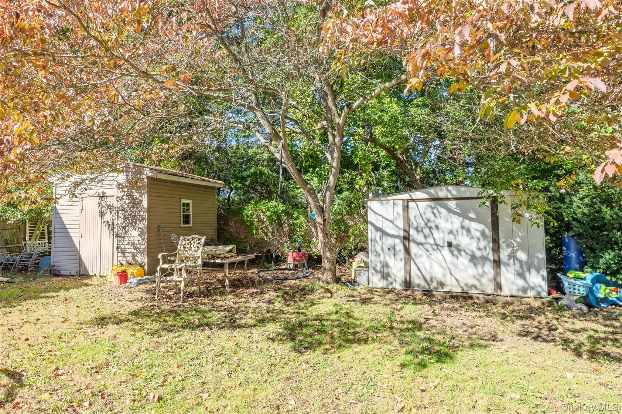 Backyard area featuring two storage structures, a mature tree, and perimeter vegetation Backyard area featuring two storage structures, a mature tree, and perimeter vegetation