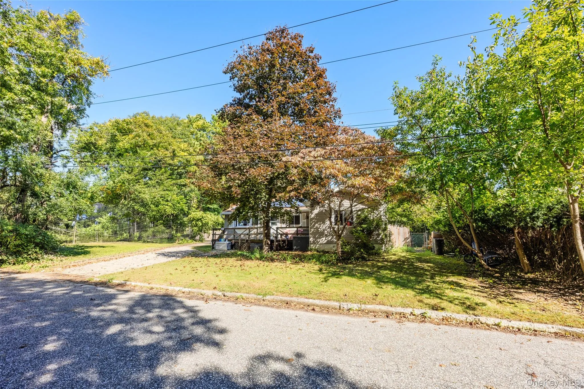 Exterior featuring a raised wood deck, gravel driveway, and mature landscaping on a grass lot Exterior featuring a raised wood deck, gravel driveway, and mature landscaping on a grass lot
