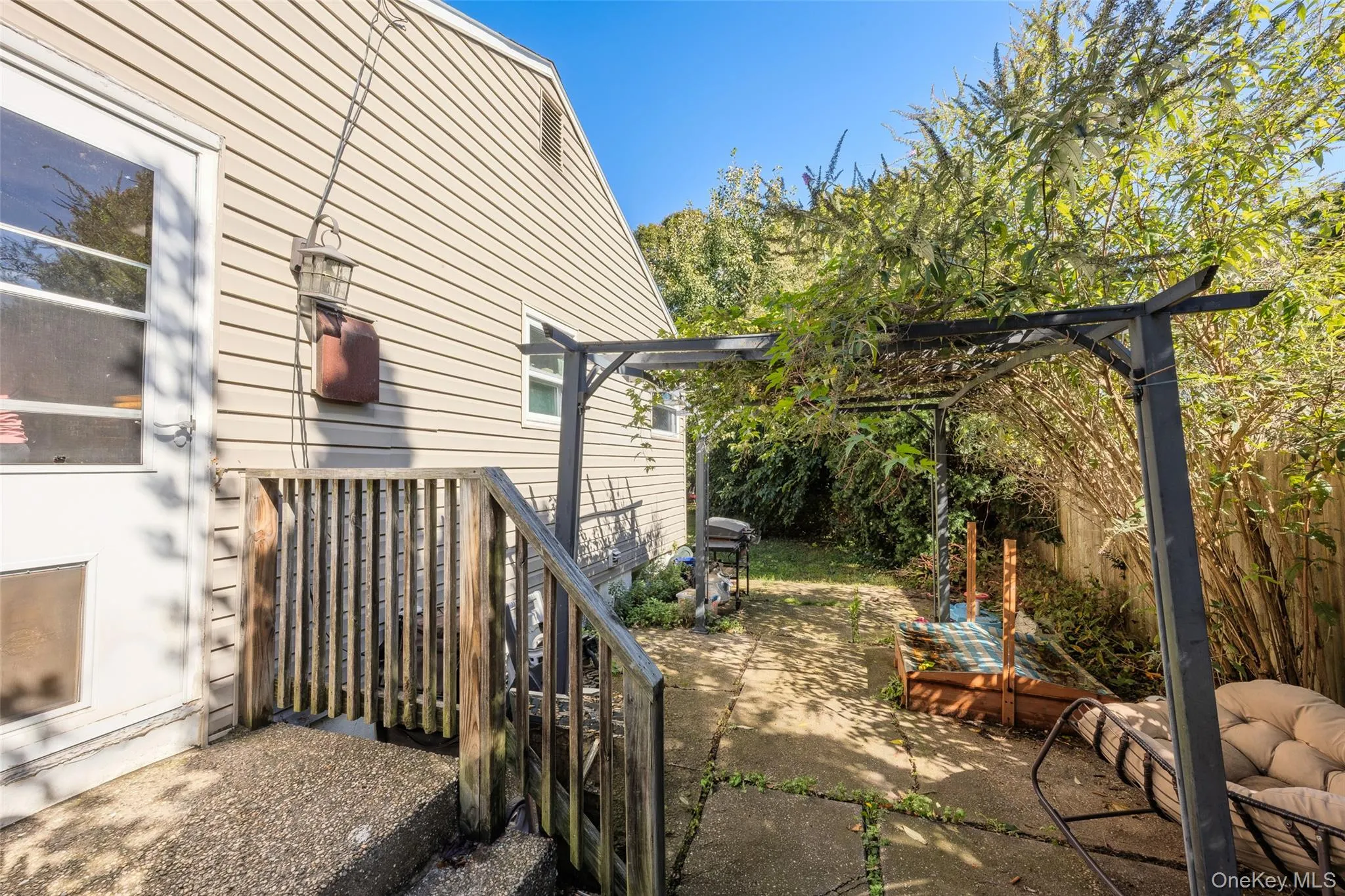 Rear exterior featuring light-colored horizontal siding, a wood-railing staircase, a paved patio area, and a metal-frame pergola Rear exterior featuring light-colored horizontal siding, a wood-railing staircase, a paved patio area, and a metal-frame pergola