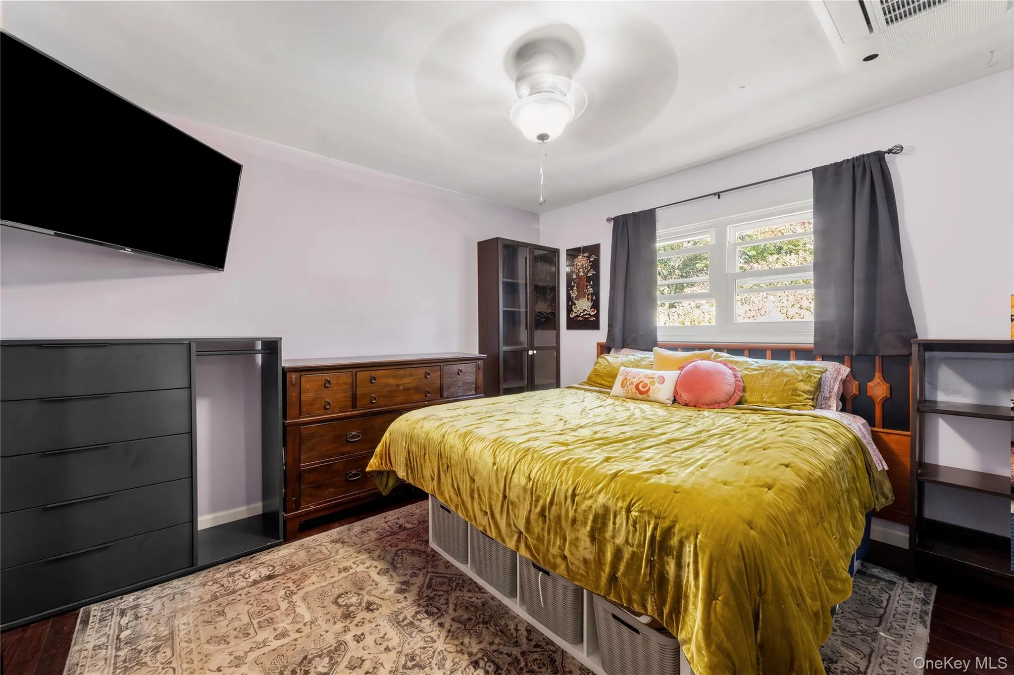 Room featuring dark-toned wood-finish flooring, a double-hung window with decorative trim, and a ceiling-mounted light fixture with an integrated fan (Decluttered Edit) Room featuring dark-toned wood-finish flooring, a double-hung window with decorative trim, and a ceiling-mounted light fixture with an integrated fan (Decluttered Edit)